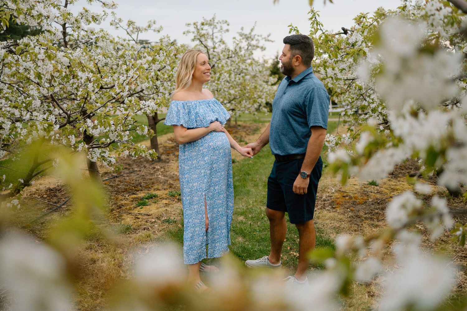 Springtime joy at Robinette’s Apple Haus. Grand Rapids maternity photographer. A glowing couple shares a sweet moment holding hands.