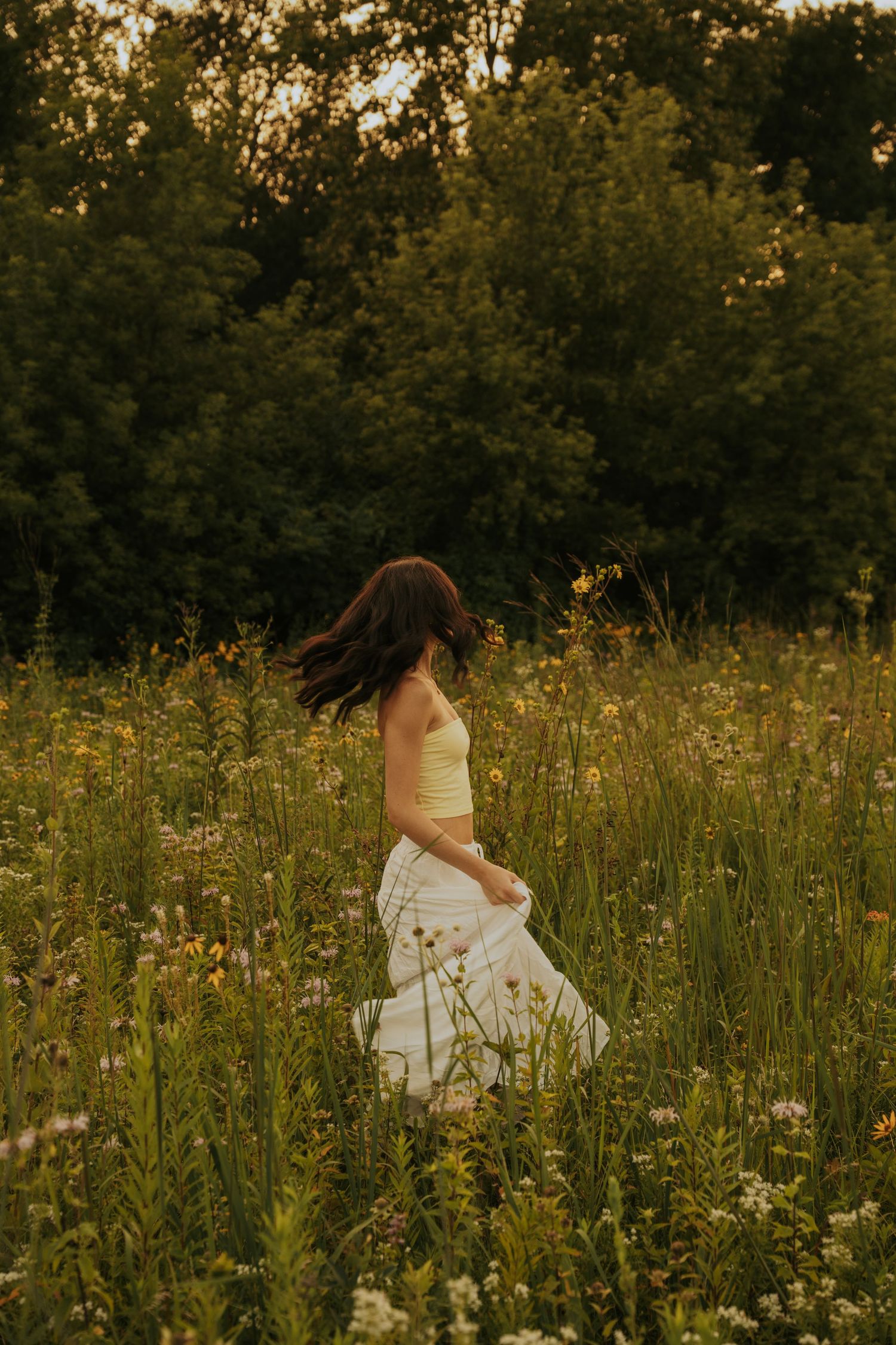 A person in a white dress spins through a golden wildflower meadow at sunset.