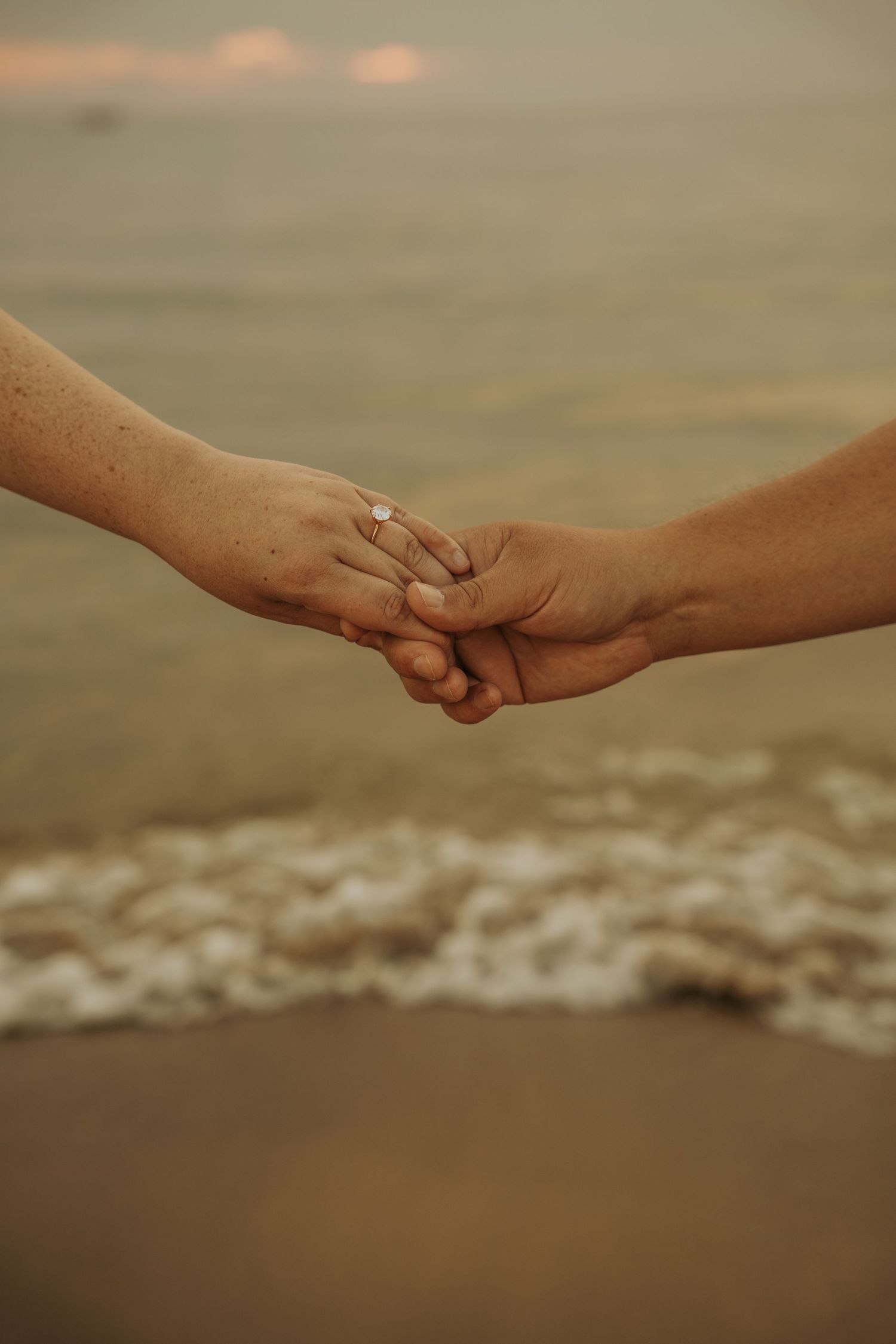 Two hands gently letting go of each other against a blurred beach background at sunset.