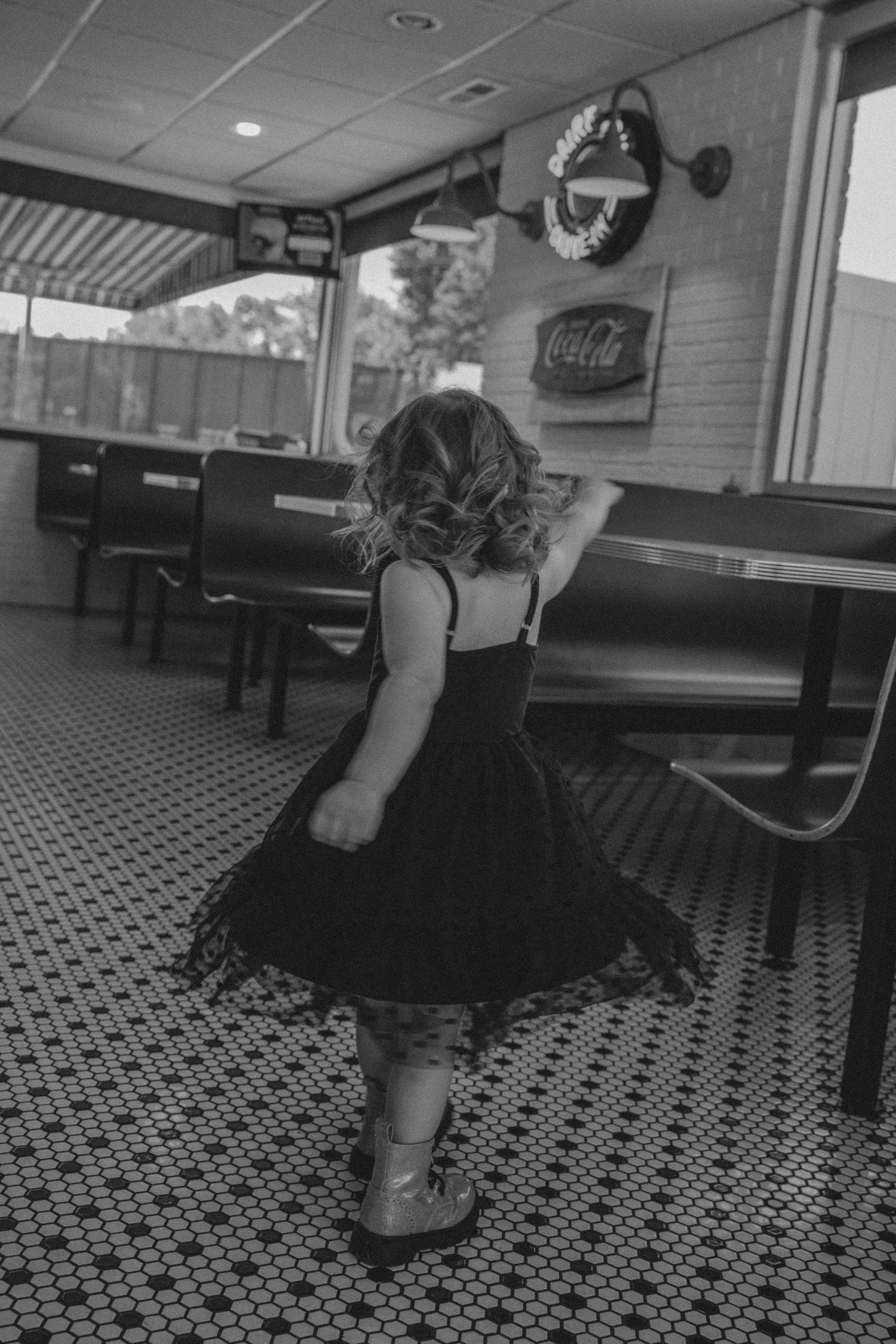 Black and white photo series showing someone in vintage-style dress dancing on a retro diner's checkered floor pattern.