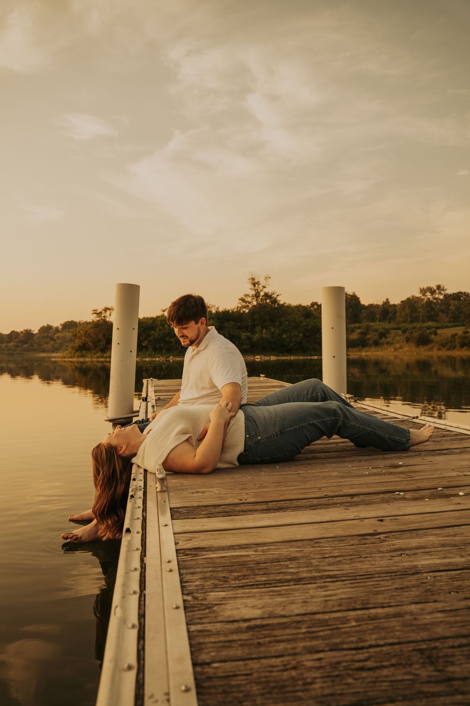 A couple lying on a wooden dock at sunset creates a romantic silhouette against the peaceful water.