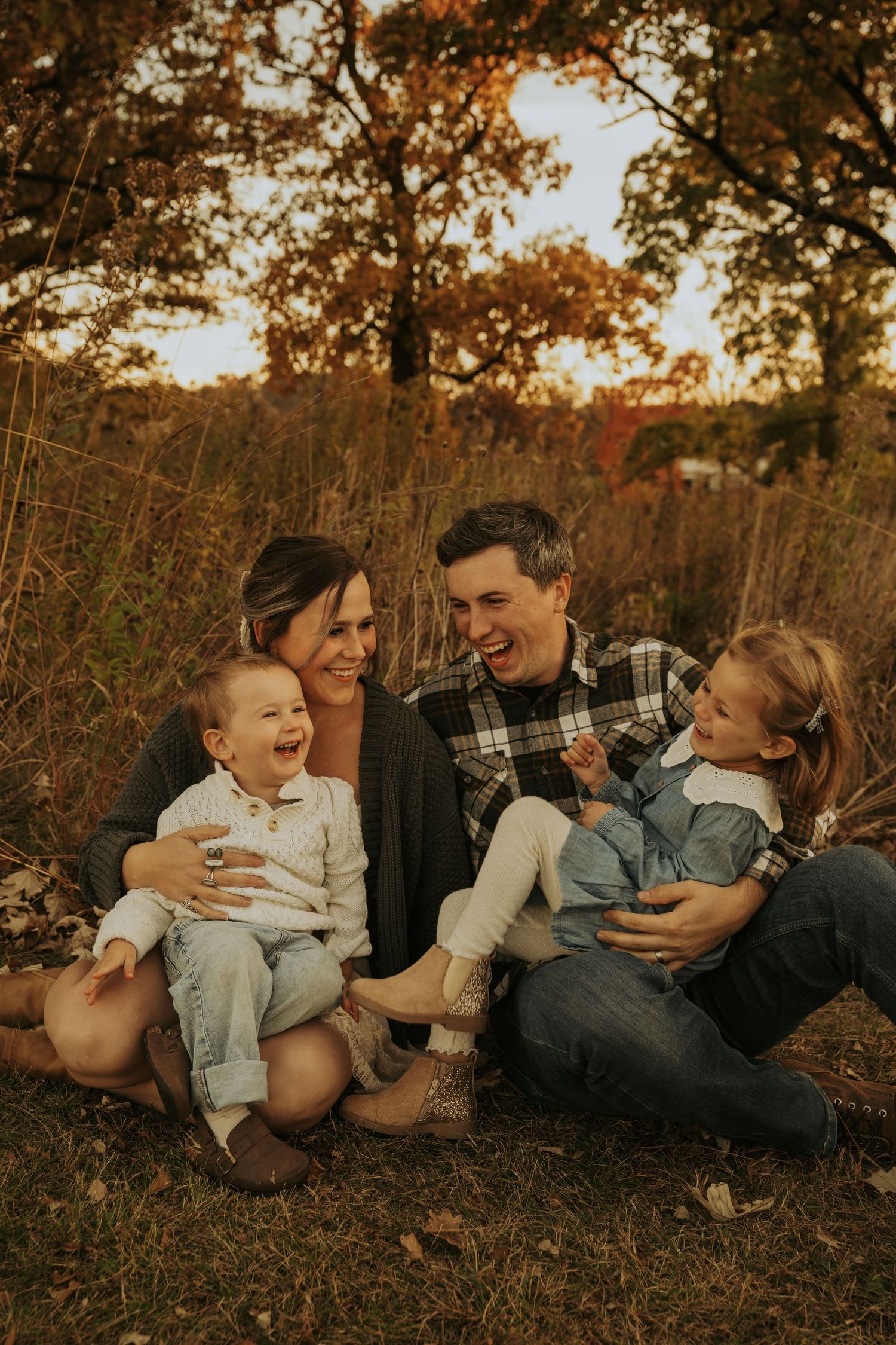 A family shares joyful laughter while laying together on autumn leaves during a golden hour photoshoot.