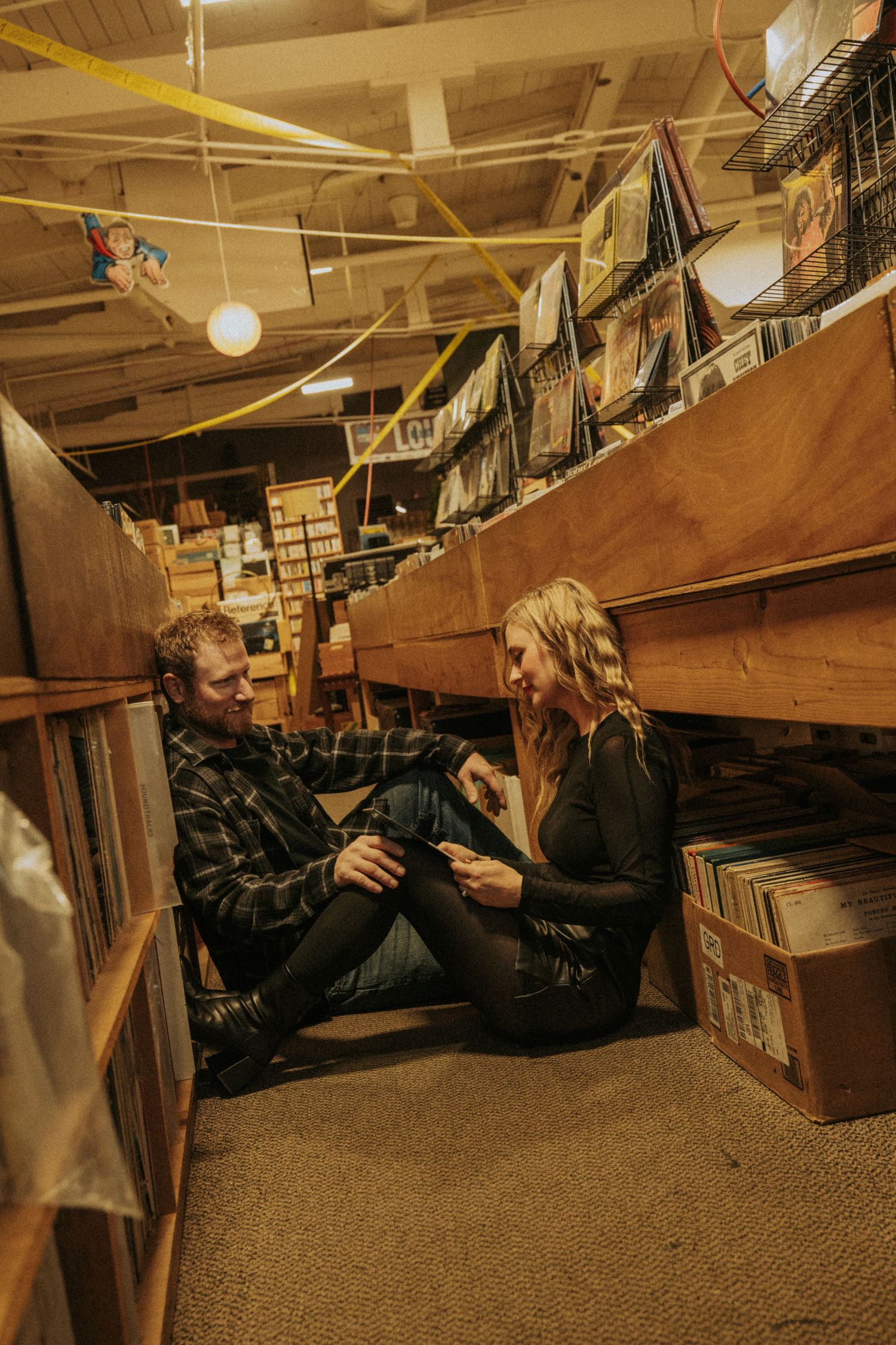 Person lying on floor in dimly lit library browsing through books and vinyl records.