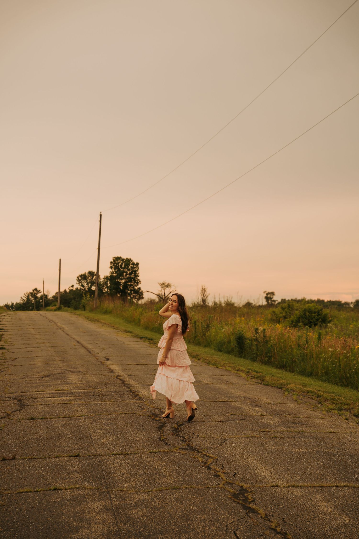 A figure in a white dress walks down a cracked rural road at sunset, creating a dreamy atmospheric scene.