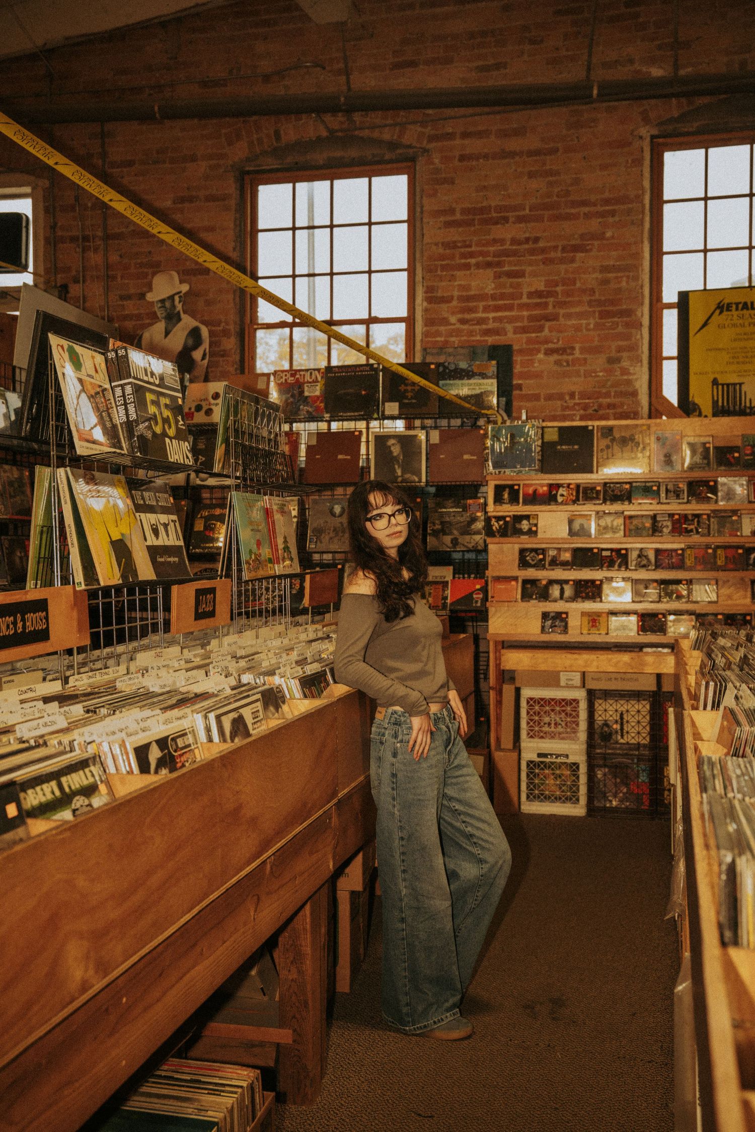 Interior view of a vintage record store with wooden bins and exposed brick walls displaying vinyl albums and music posters.