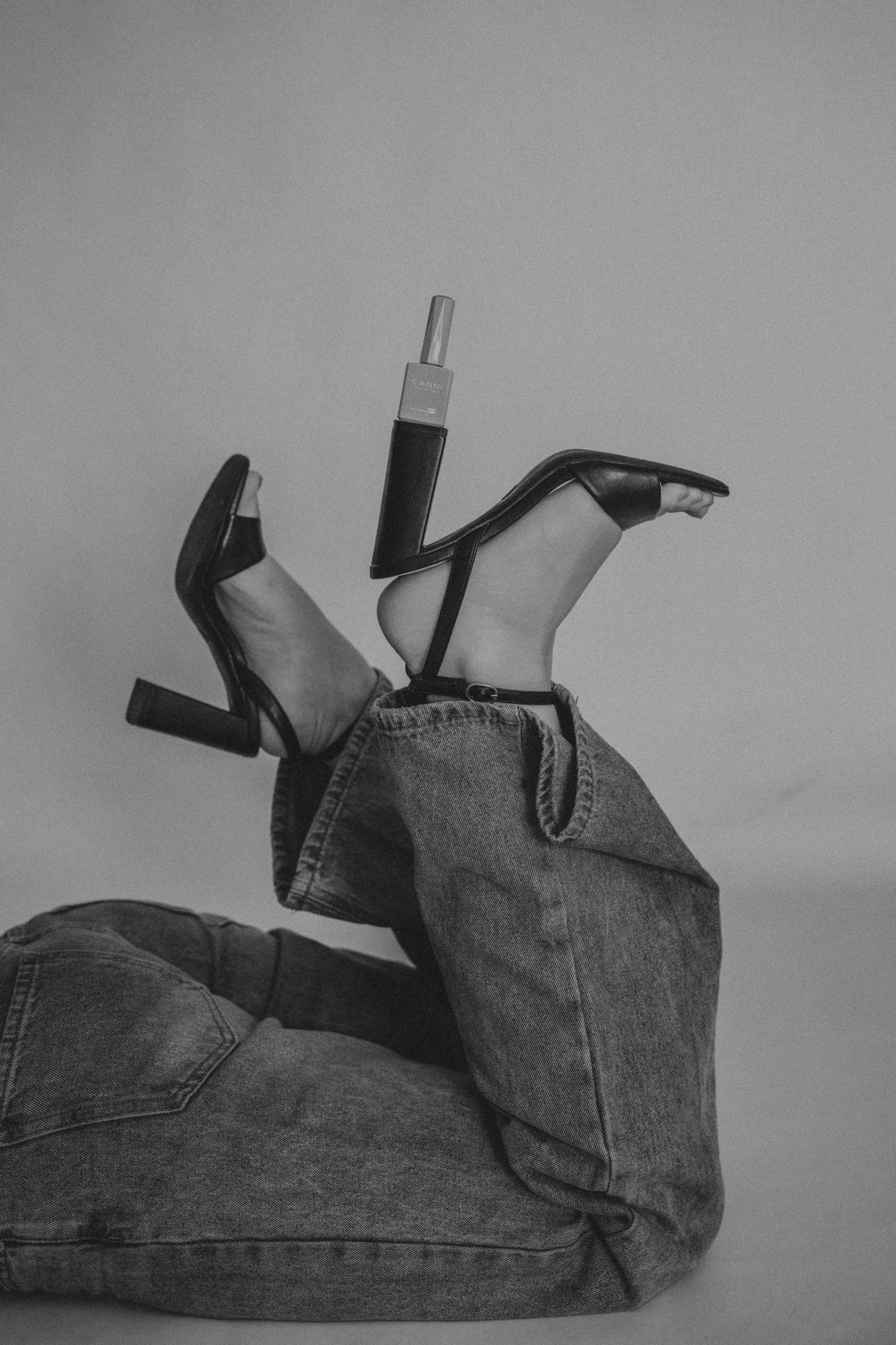 Black and white artistic photo of legs in jeans and high heels lying against a plain background.