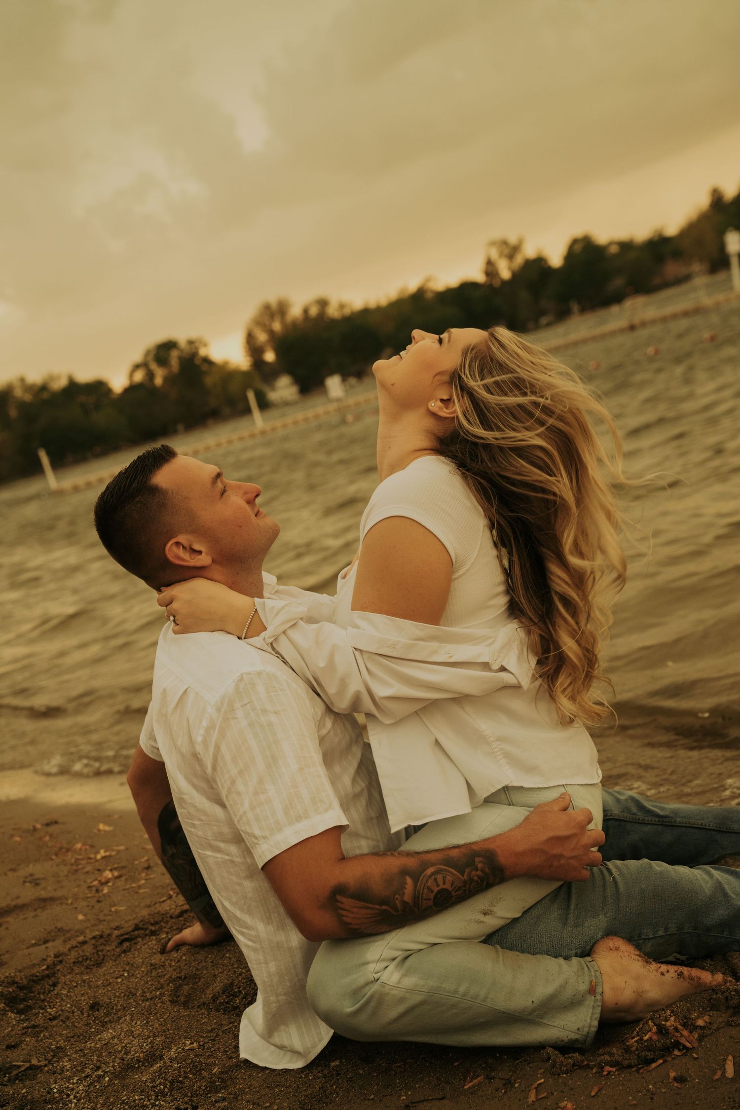 A romantic couple in white clothing embraces on a beach at sunset, creating a series of intimate poses by the water.