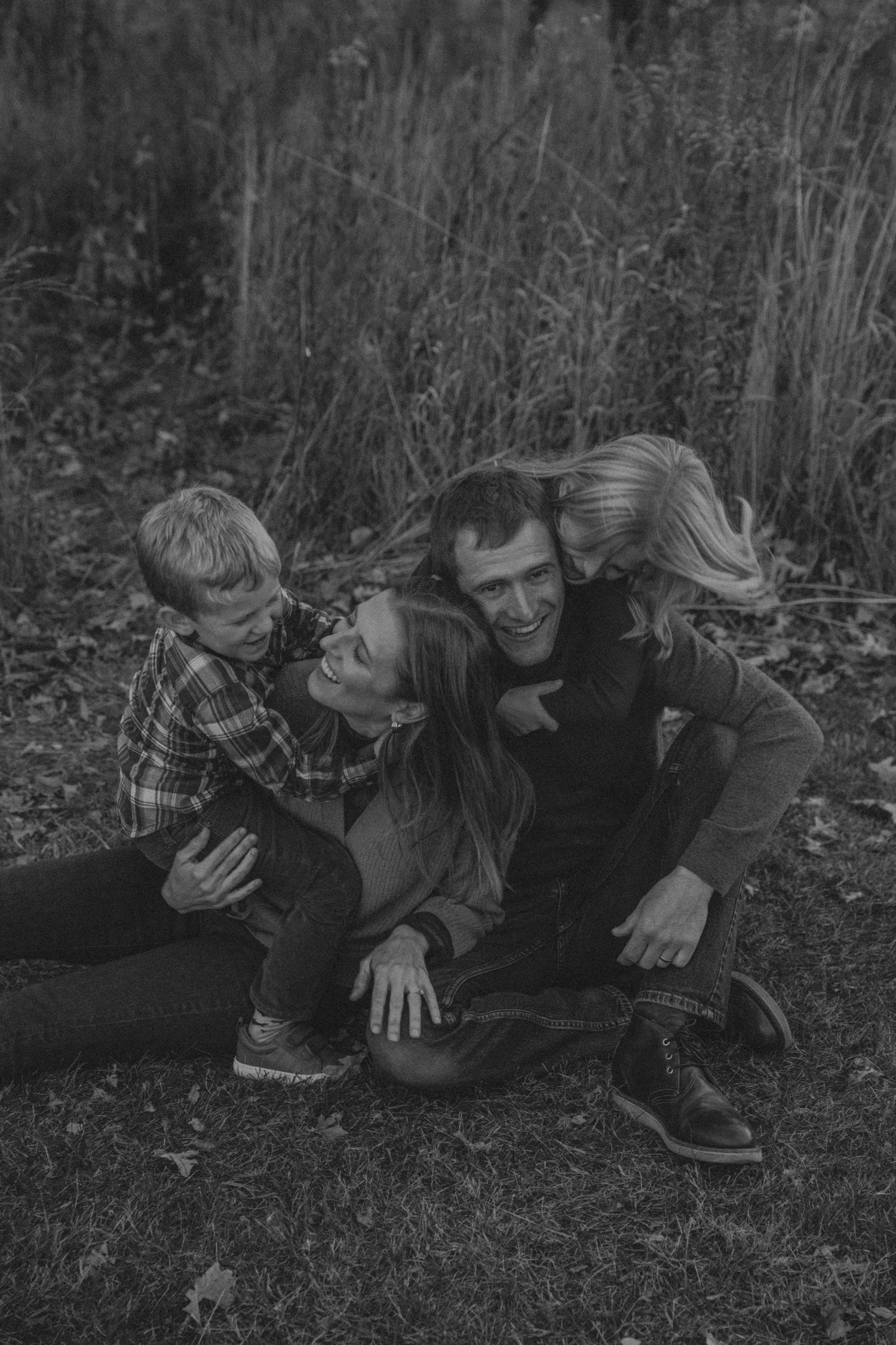 A black and white photo sequence showing three people lying down and laughing together in fallen leaves outdoors.