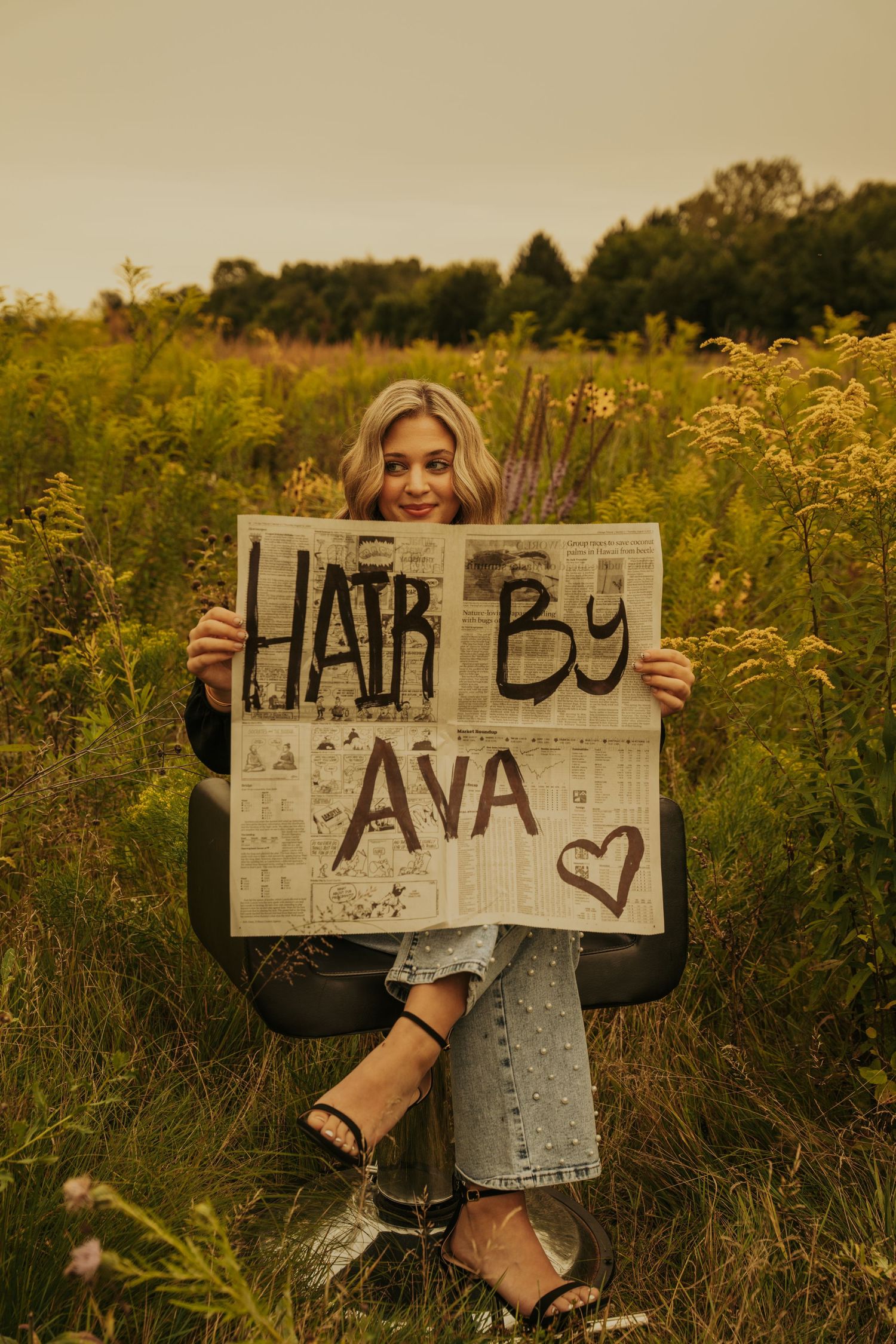 Person holding handwritten sign in golden wildflower field at sunset with artistic rustic aesthetic.