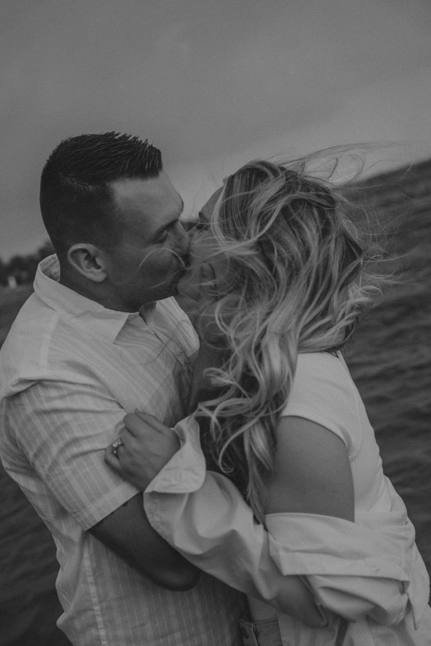 Black and white romantic portrait of a couple embracing while wind blows through her long wavy hair.