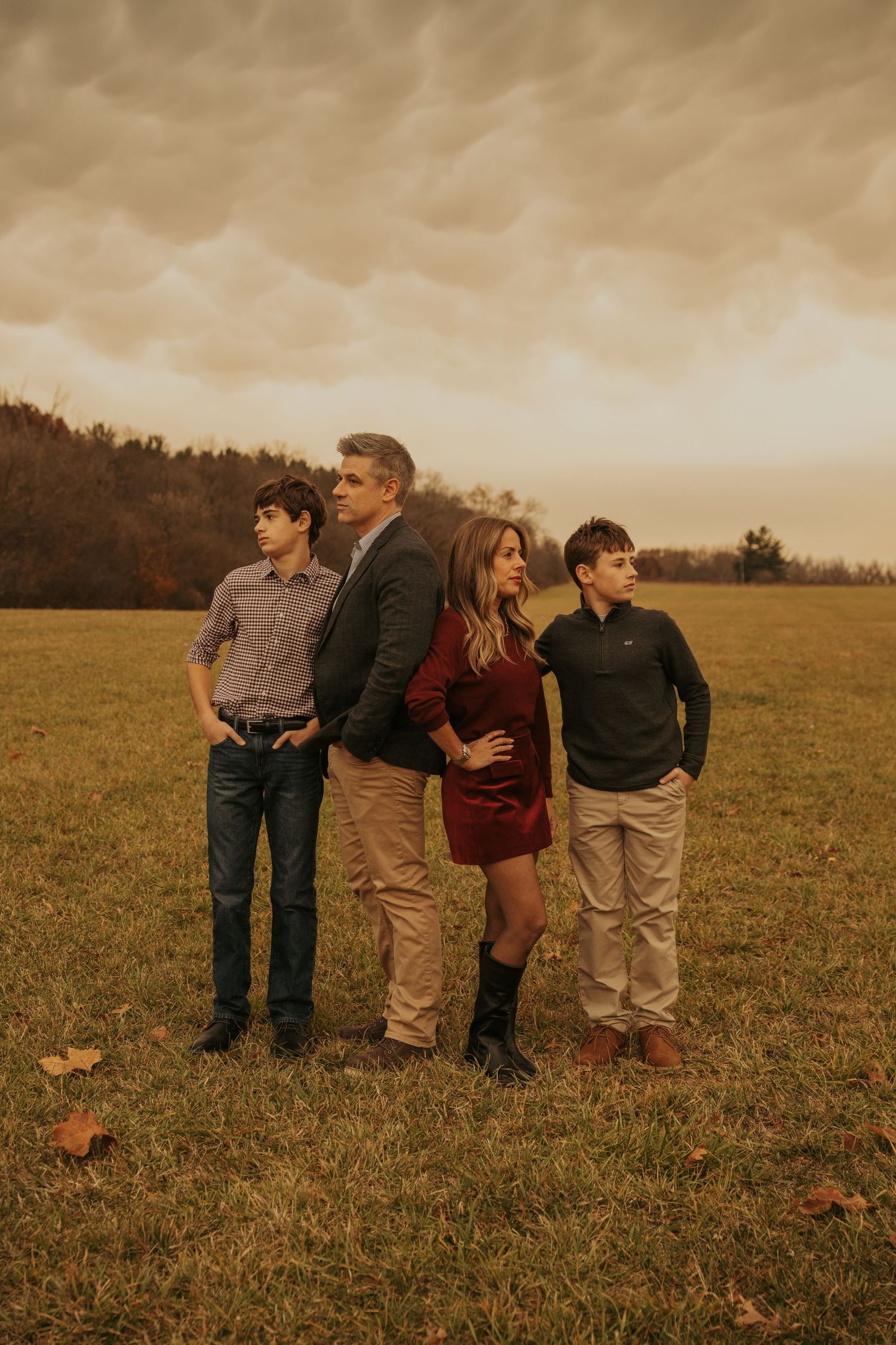 A family stands together in an open field during golden hour with a moody autumn sky in the background.