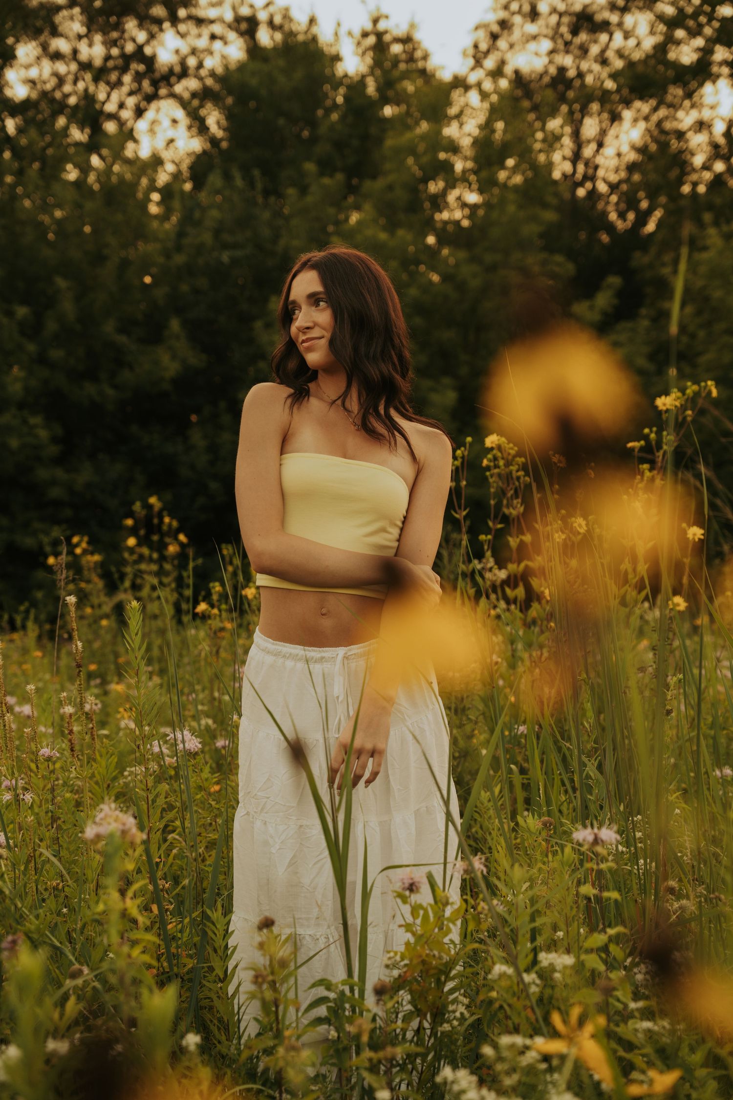 A person in a cream crop top and white skirt poses gracefully in a wildflower meadow during golden hour.