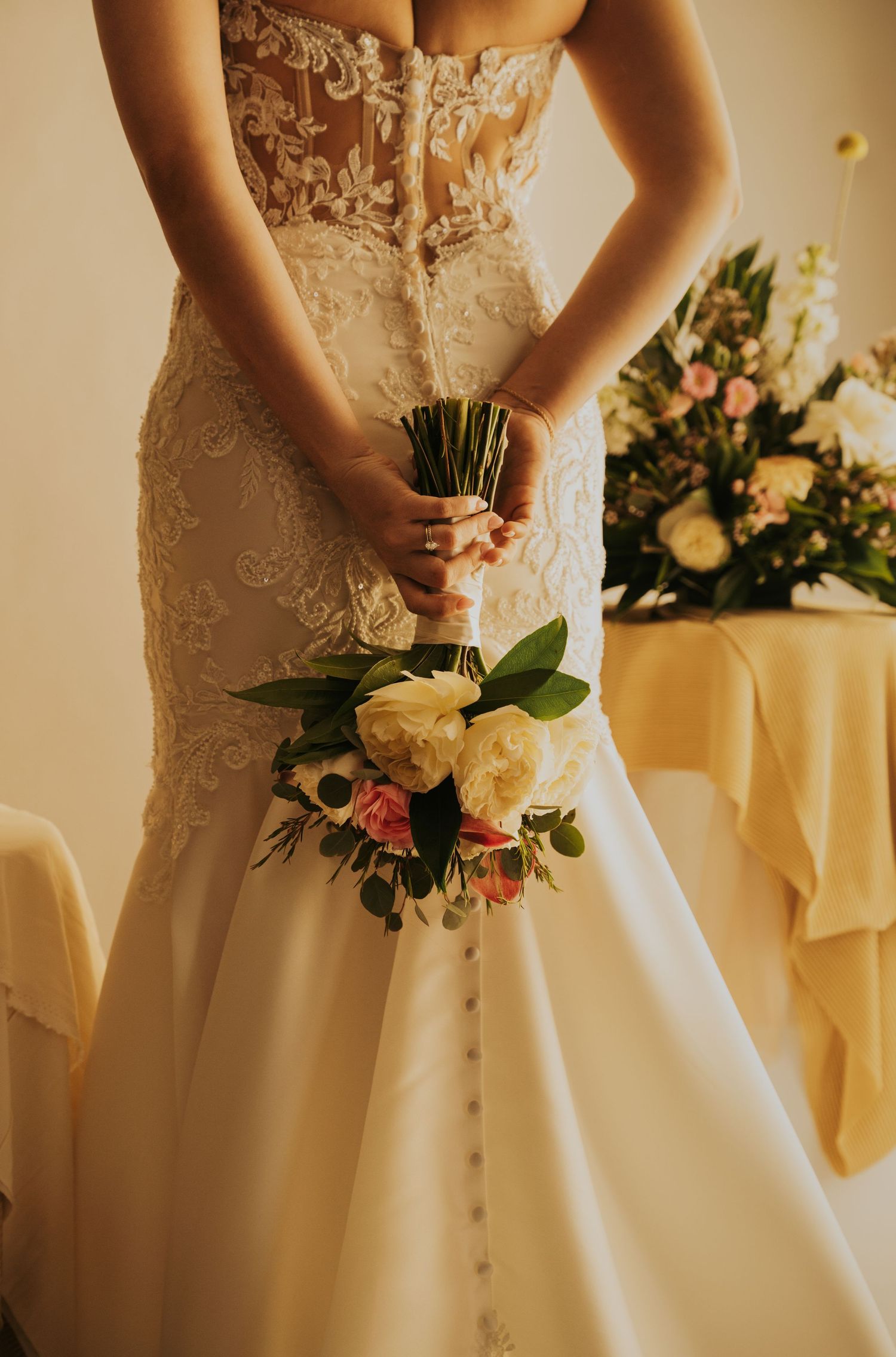 Close-up details of a bride in a white lace wedding dress holding a romantic bouquet of cream and pink flowers.