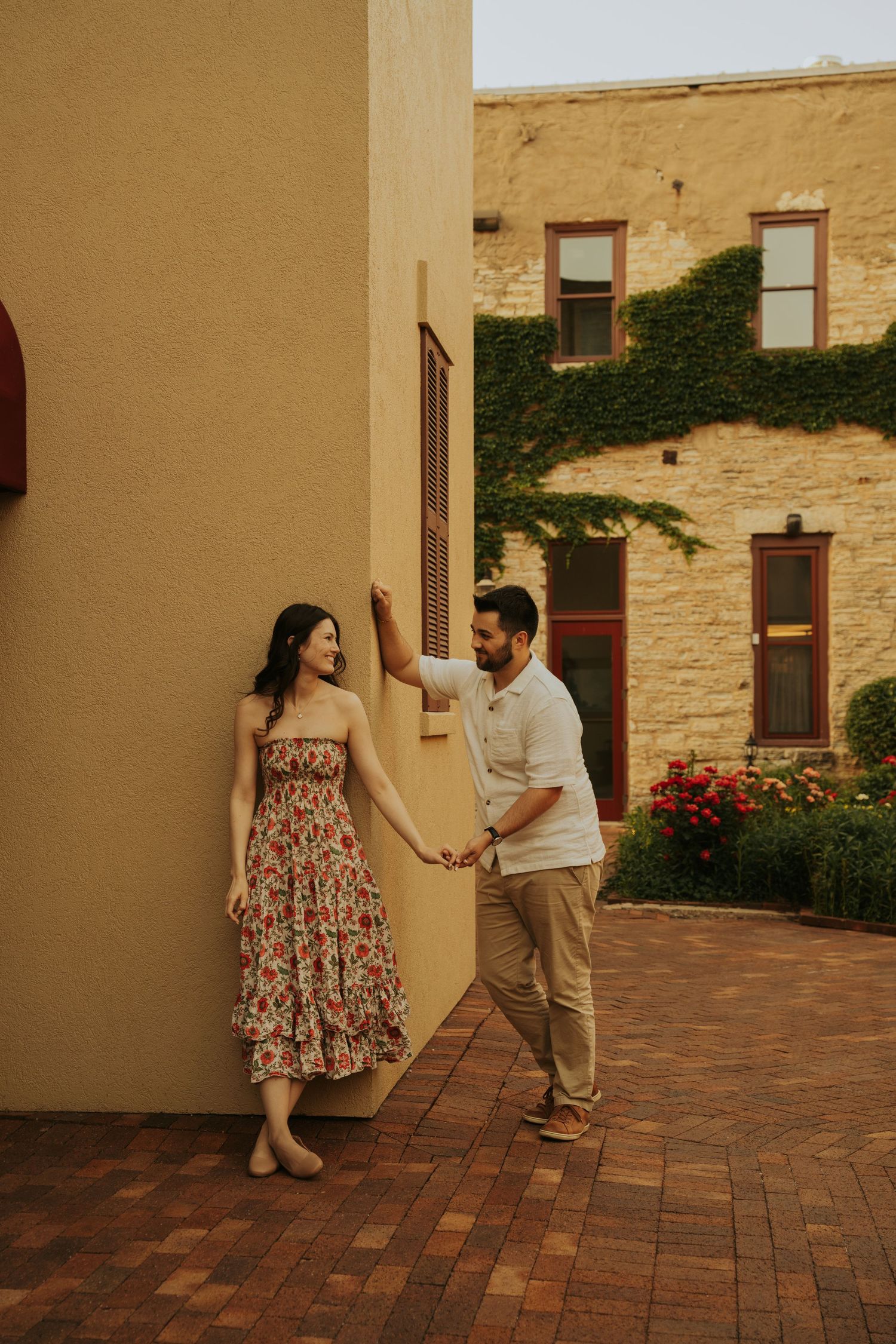 A couple in romantic poses against a beige stone wall and brick patio in warm evening light.