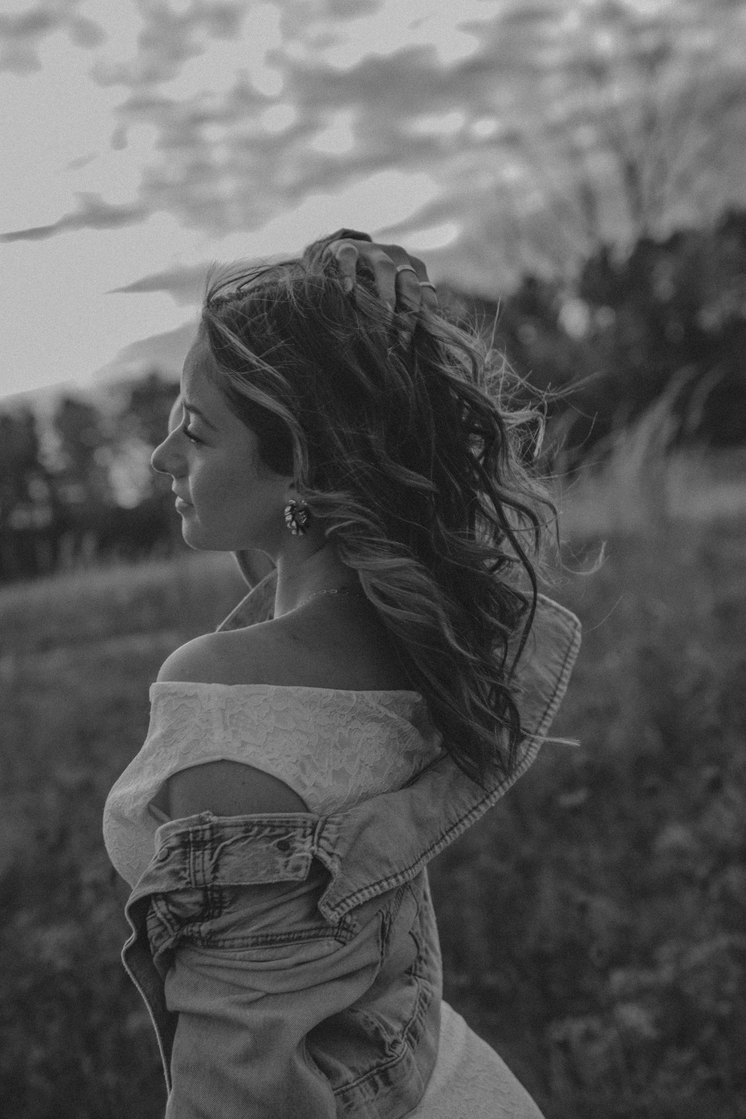 Black and white portrait of a woman with flowing hair in an off-shoulder top looking to the side in dramatic lighting.