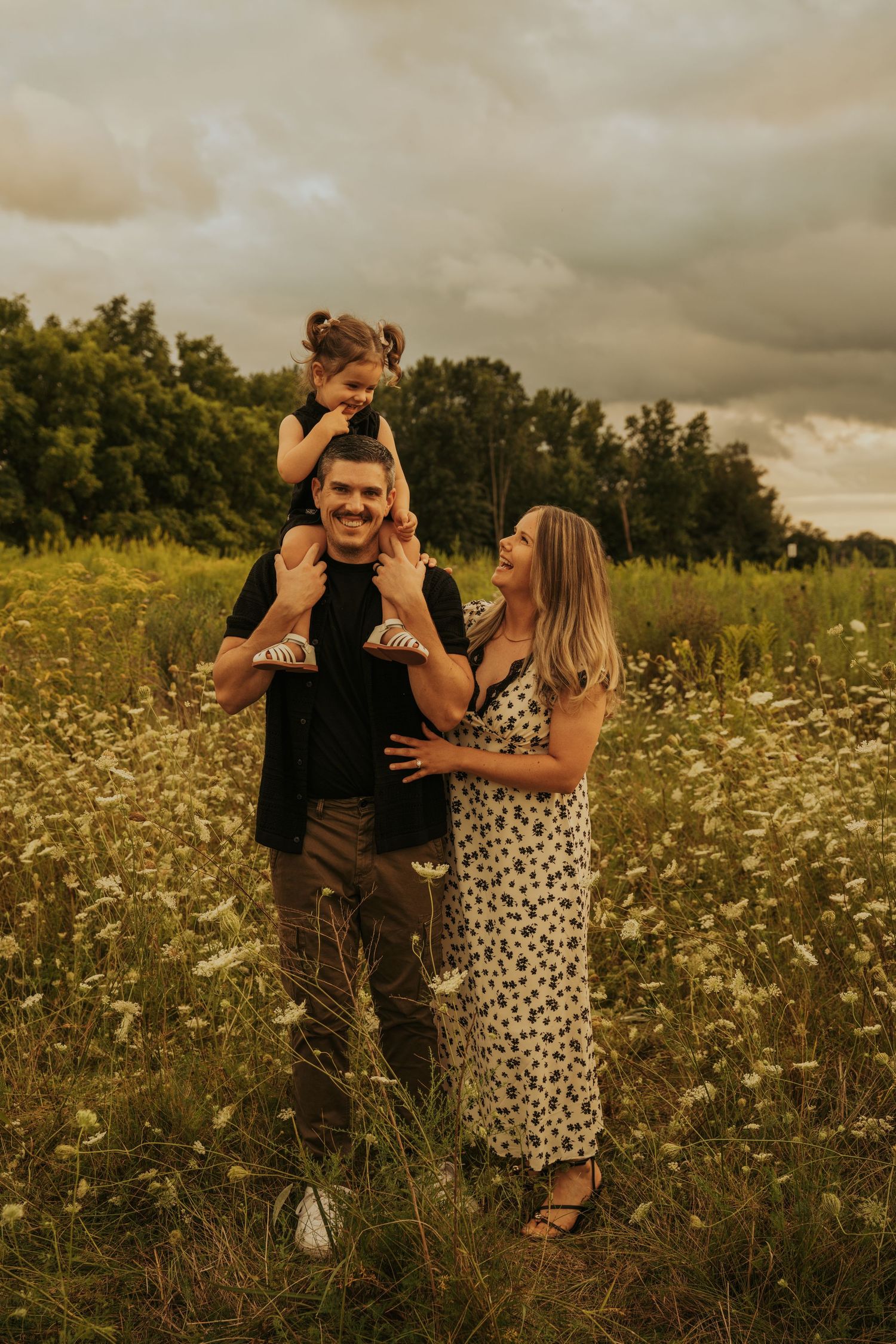 A family shares a tender moment together in a wildflower meadow at sunset with moody storm clouds overhead.