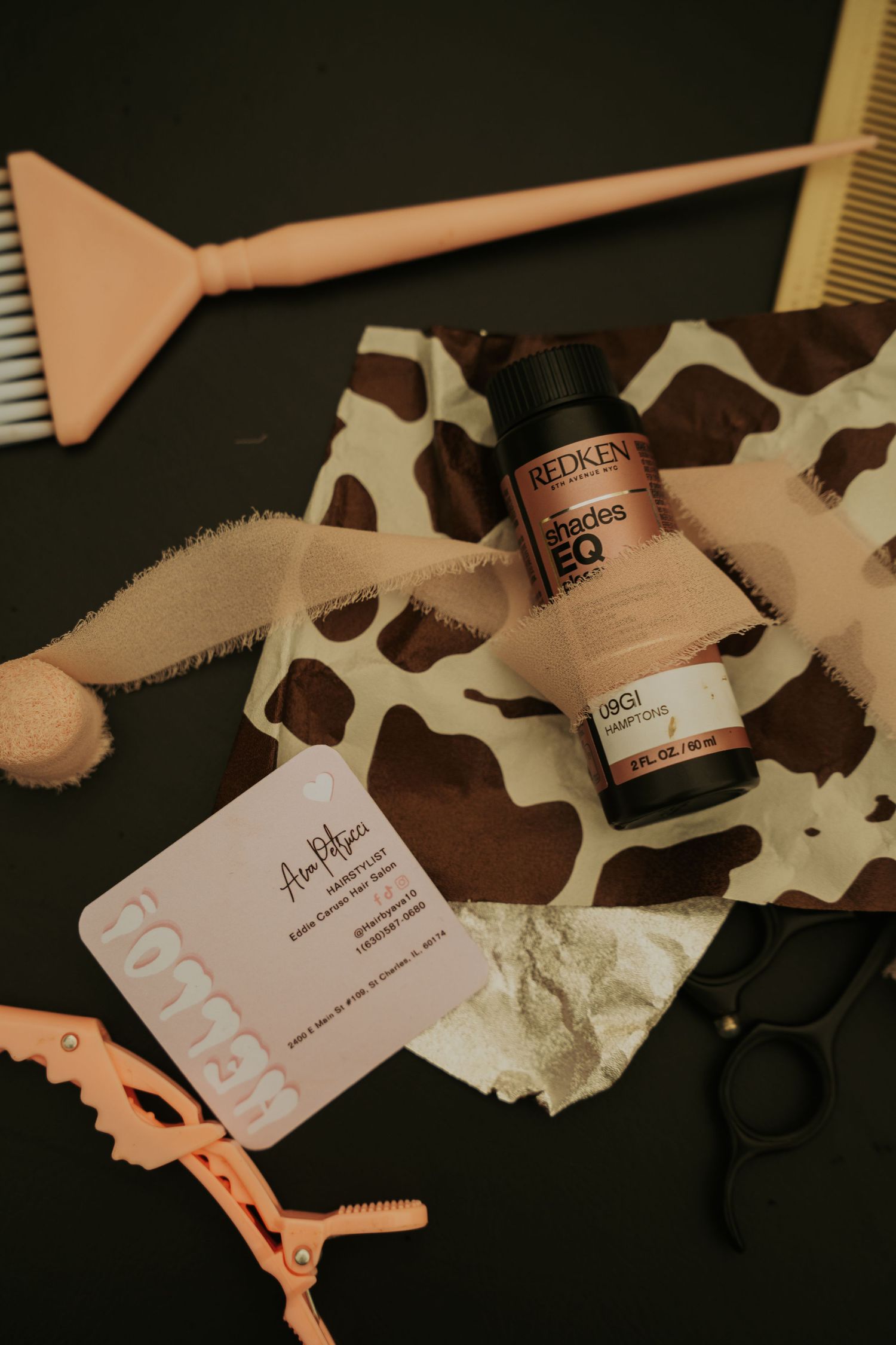 Hair styling tools and products arranged artistically on a dark background with cow print fabric elements.