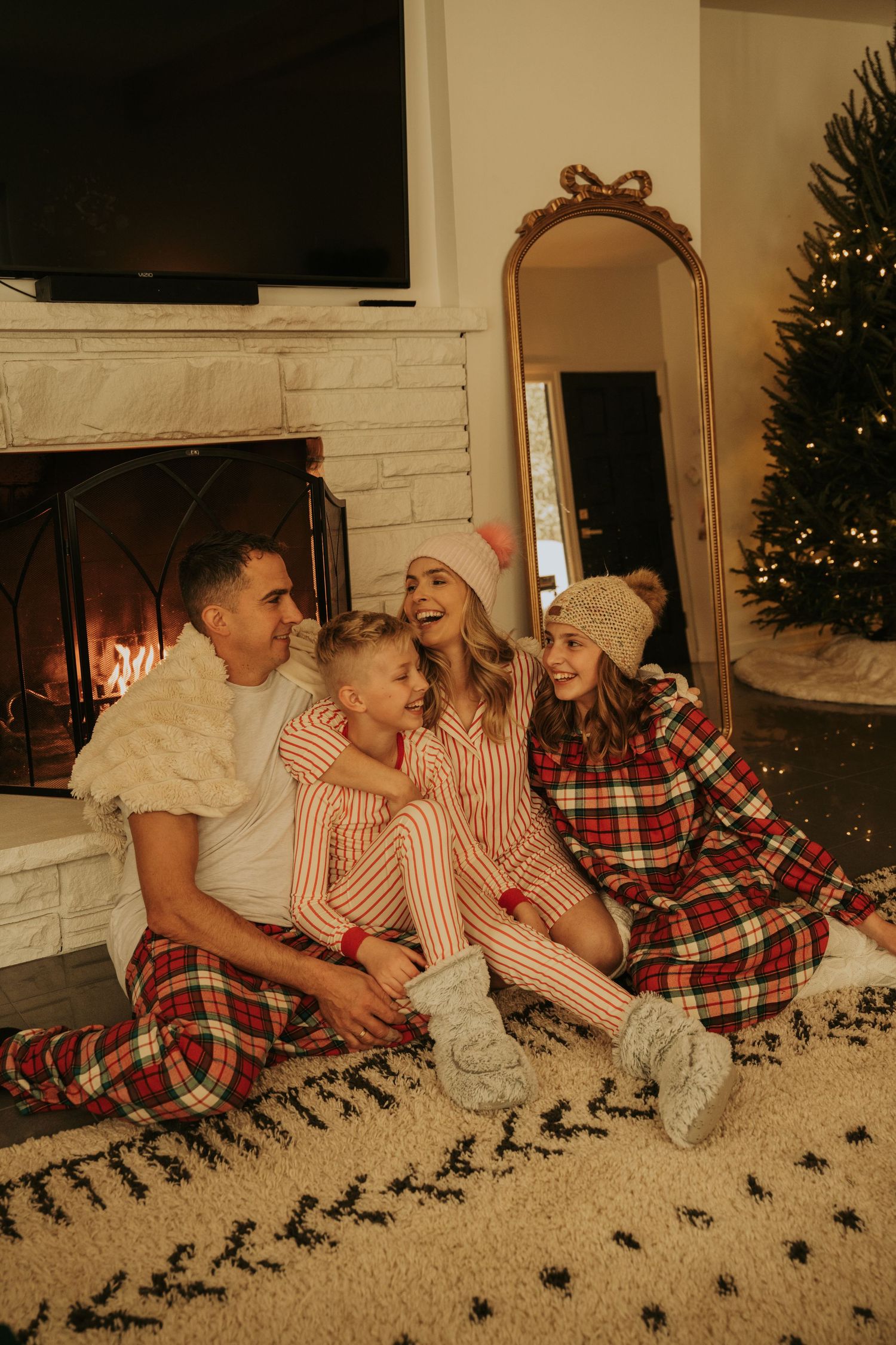 Family lying on carpet enjoying holiday moments with Christmas tree in background.