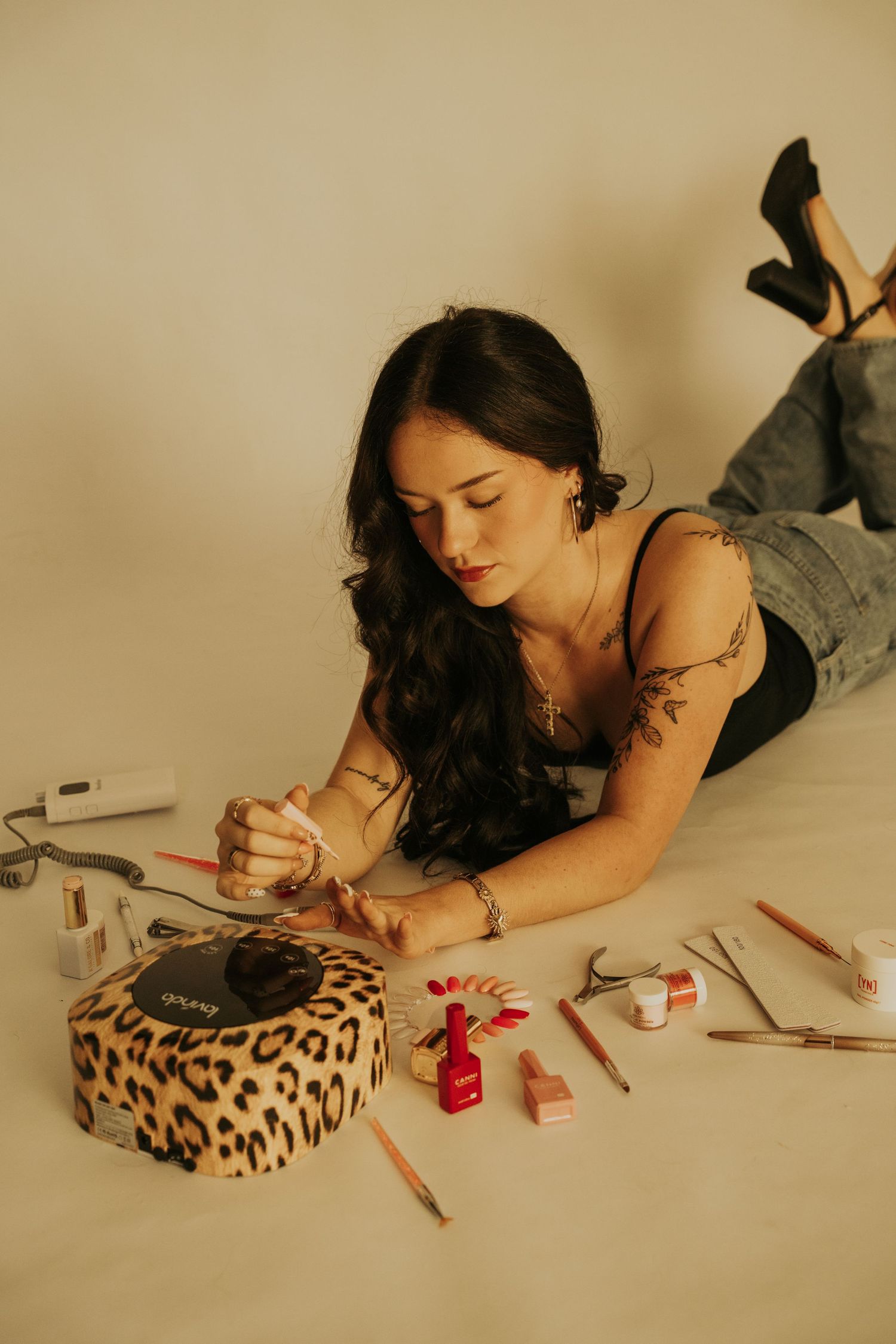 Someone lying down on a white surface painting their nails with red polish next to a leopard print pillow.