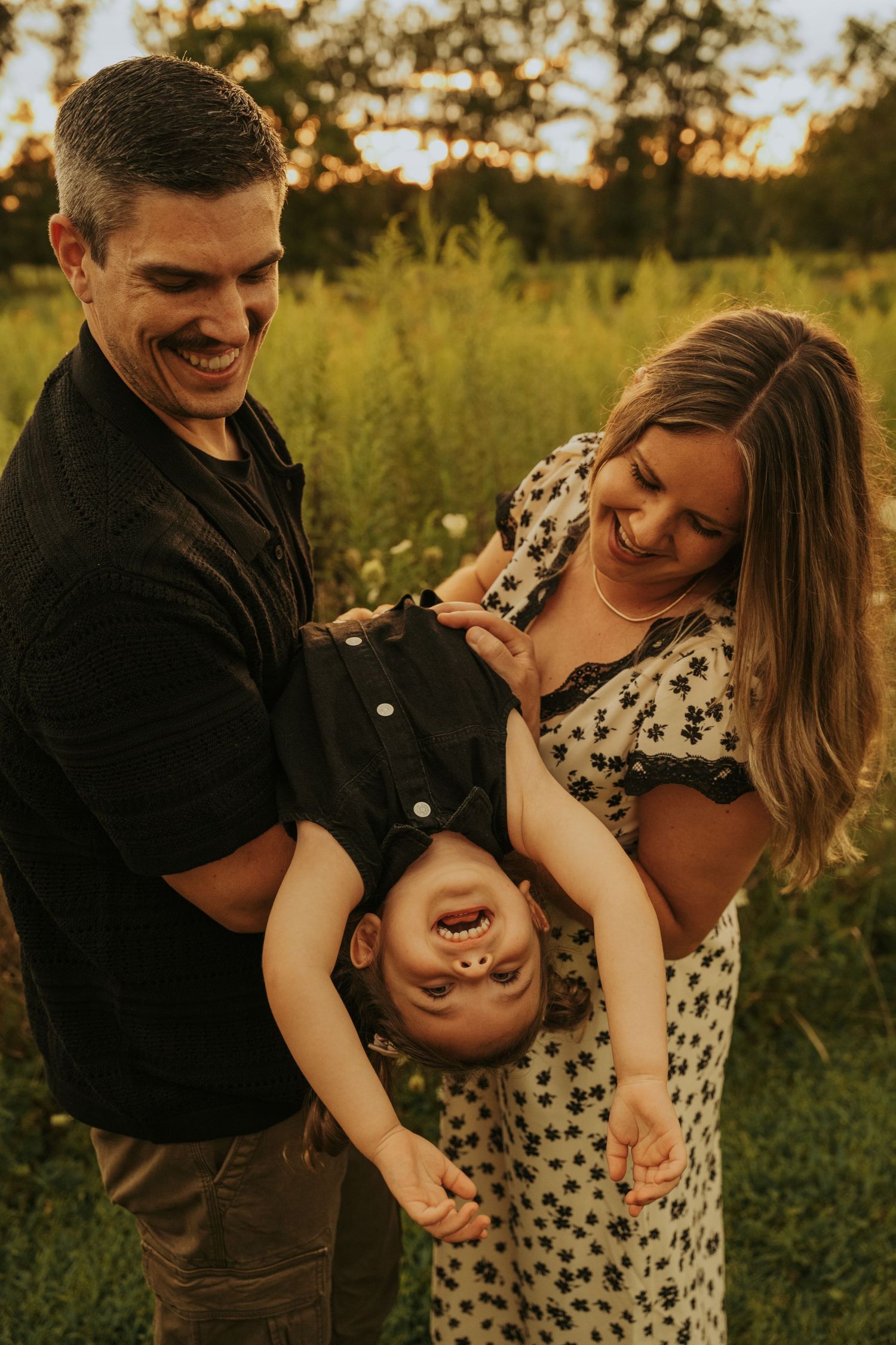 A couple shares an intimate moment in a sunlit field at golden hour while wearing casual attire.