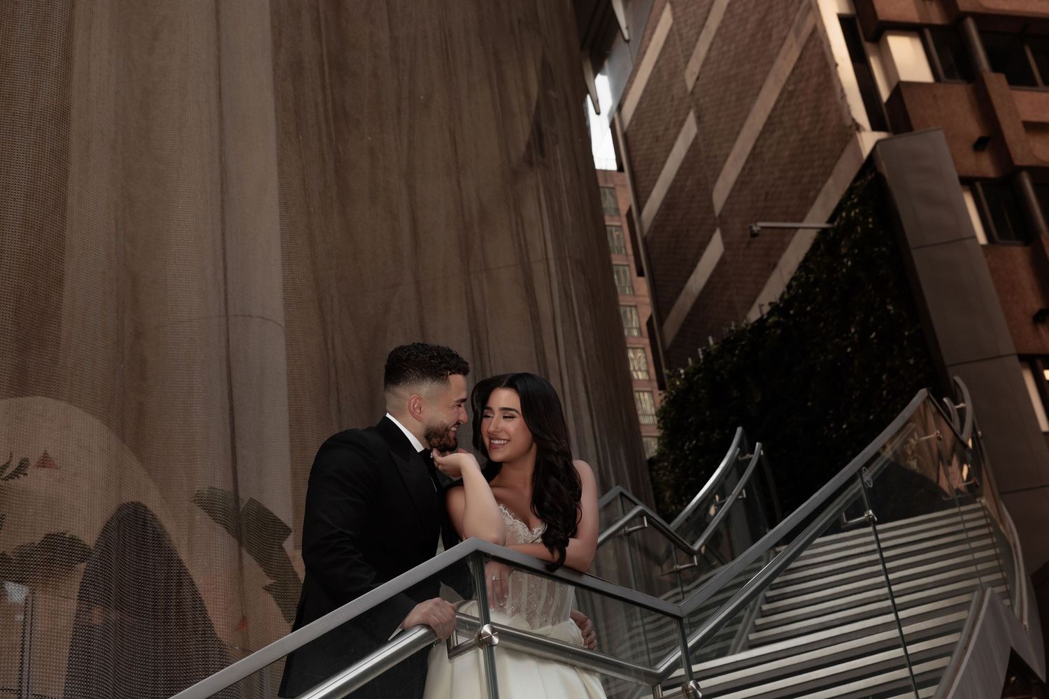Couple sharing a romantic moment on a staircase balcony during their wedding, dressed in elegant formal attire.