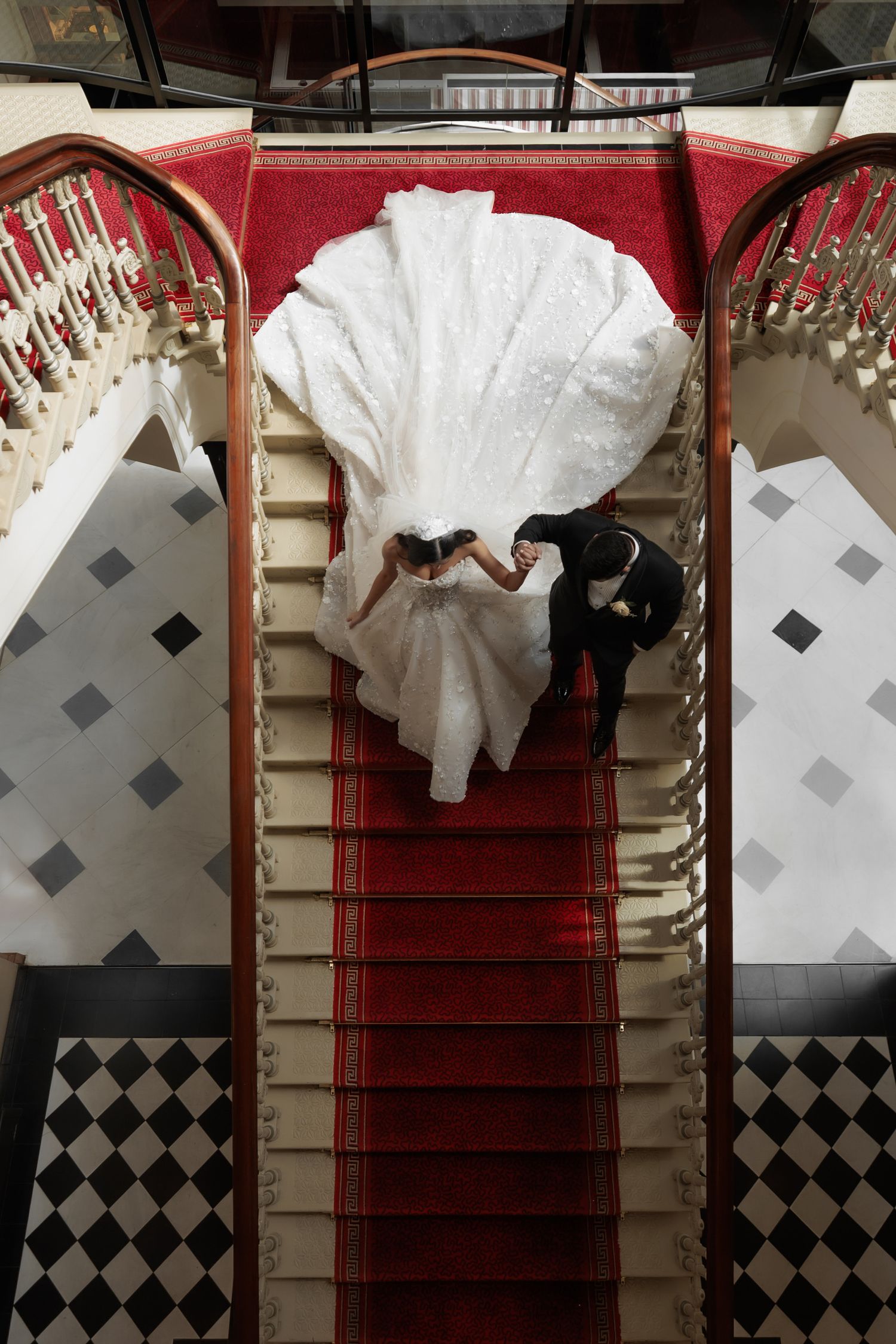 Aerial view of bride and groom descending grand staircase with red carpet, stunning white gown train fanned out beautifully.
