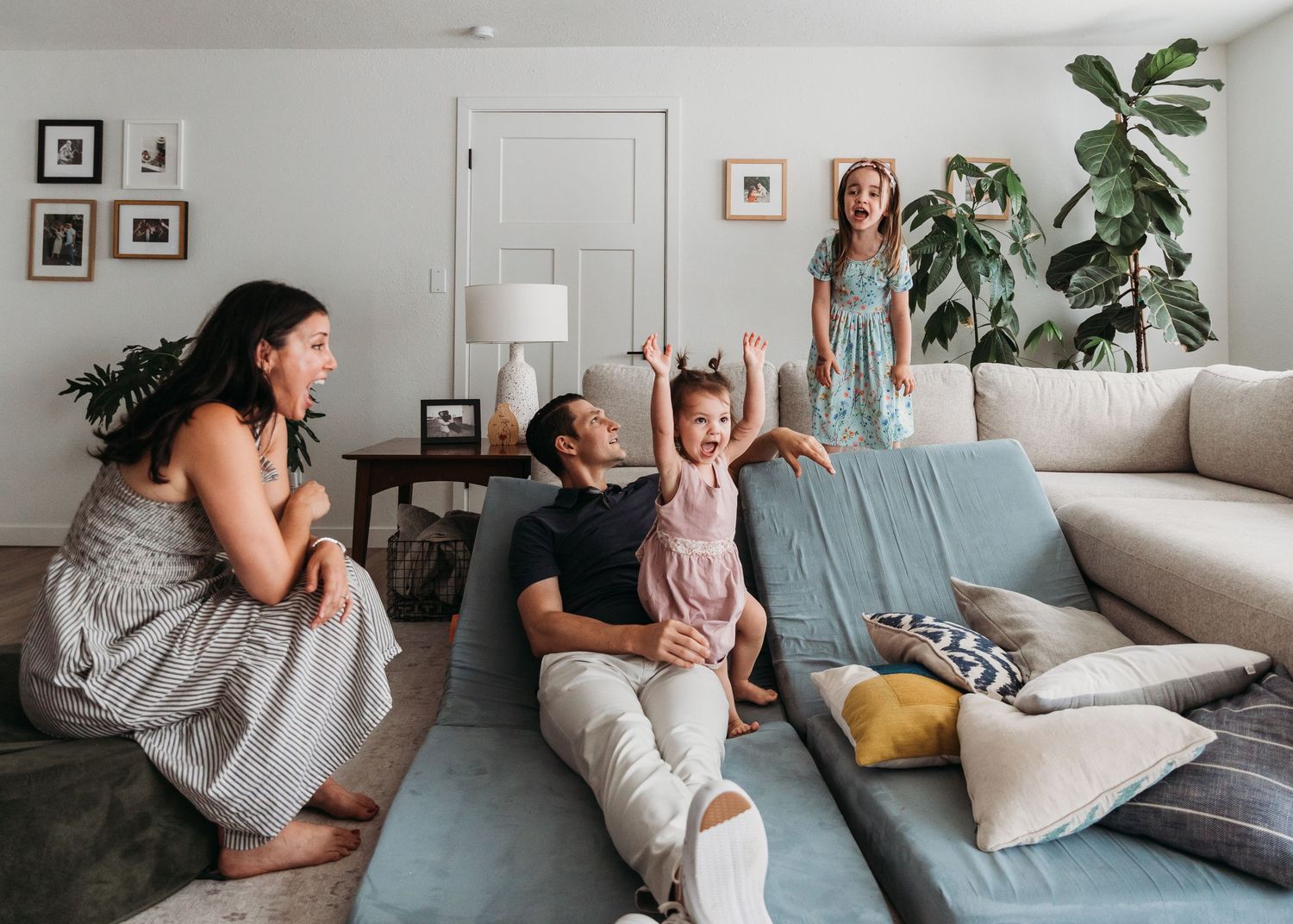 People relax together in a cozy living room with a gray sectional sofa and indoor plants.