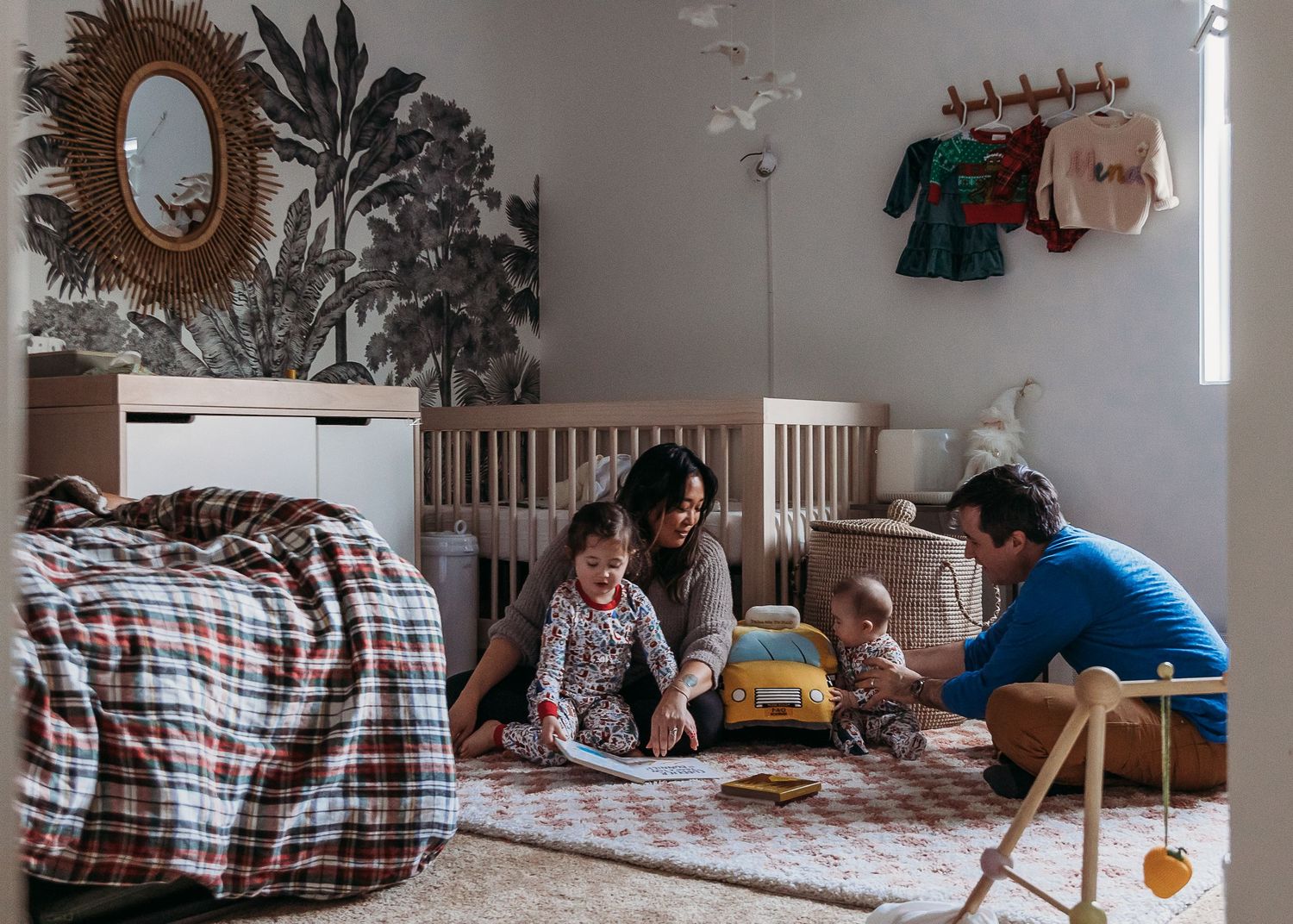 Family relaxing together on a cozy rug in a nursery room with white walls and hanging clothes.
