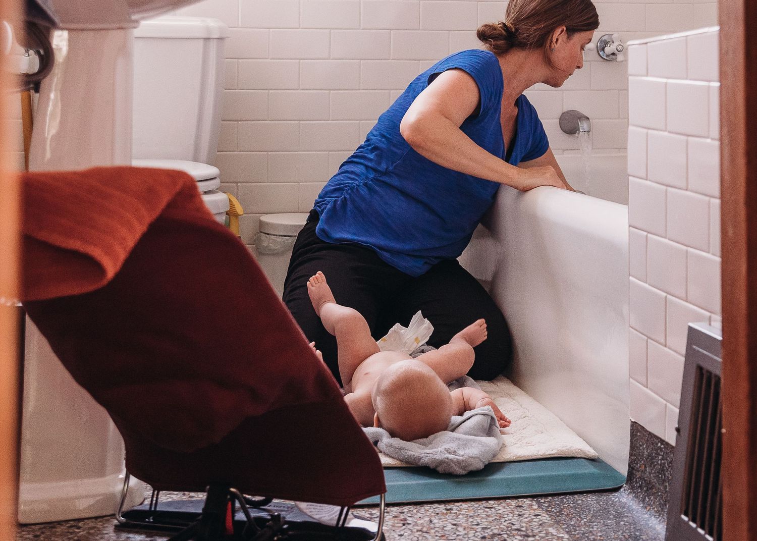A caregiver changes a baby's diaper on a changing pad in a tiled bathroom.