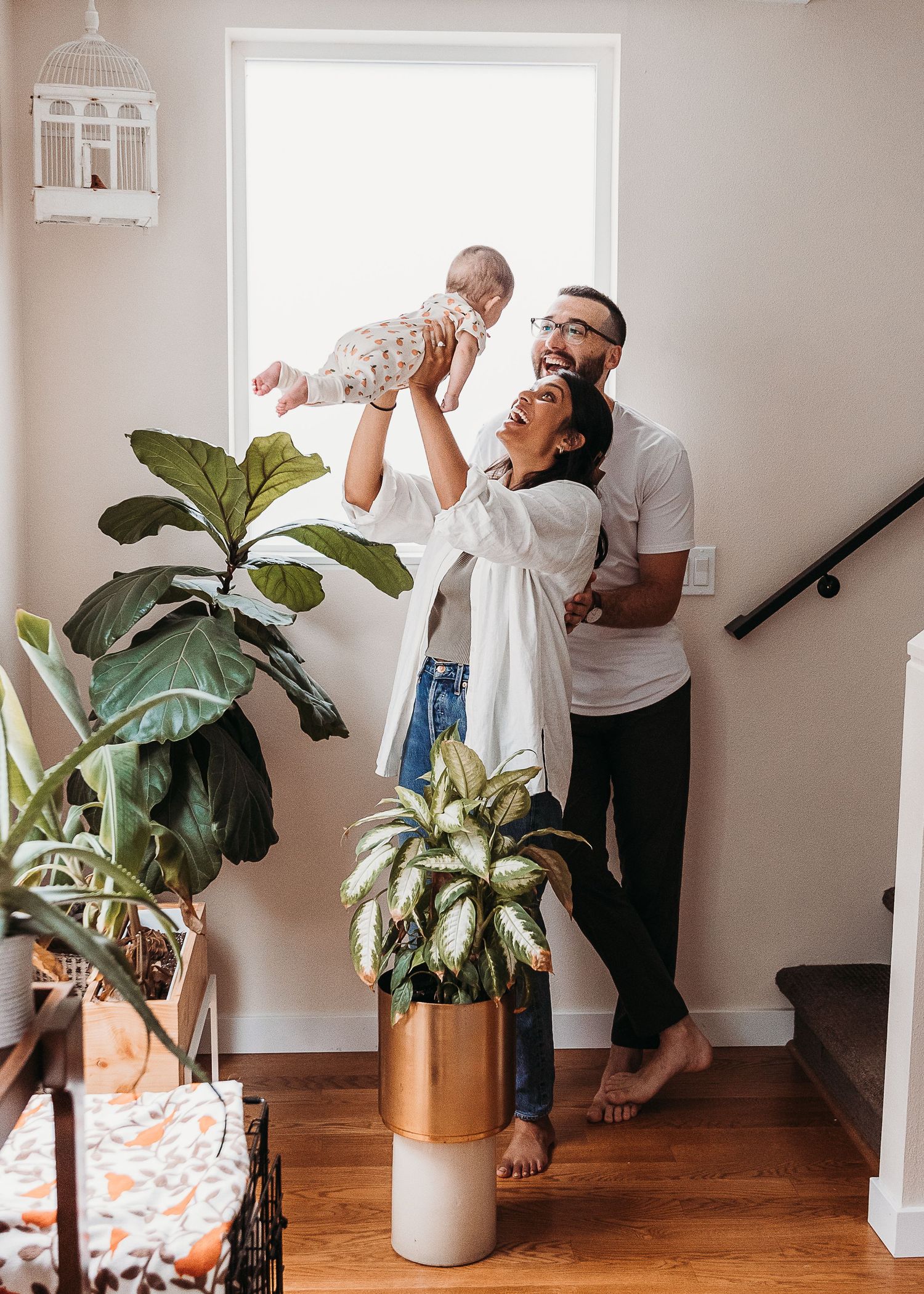A joyful family group shares a playful moment together beside indoor plants in a bright minimalist home interior.