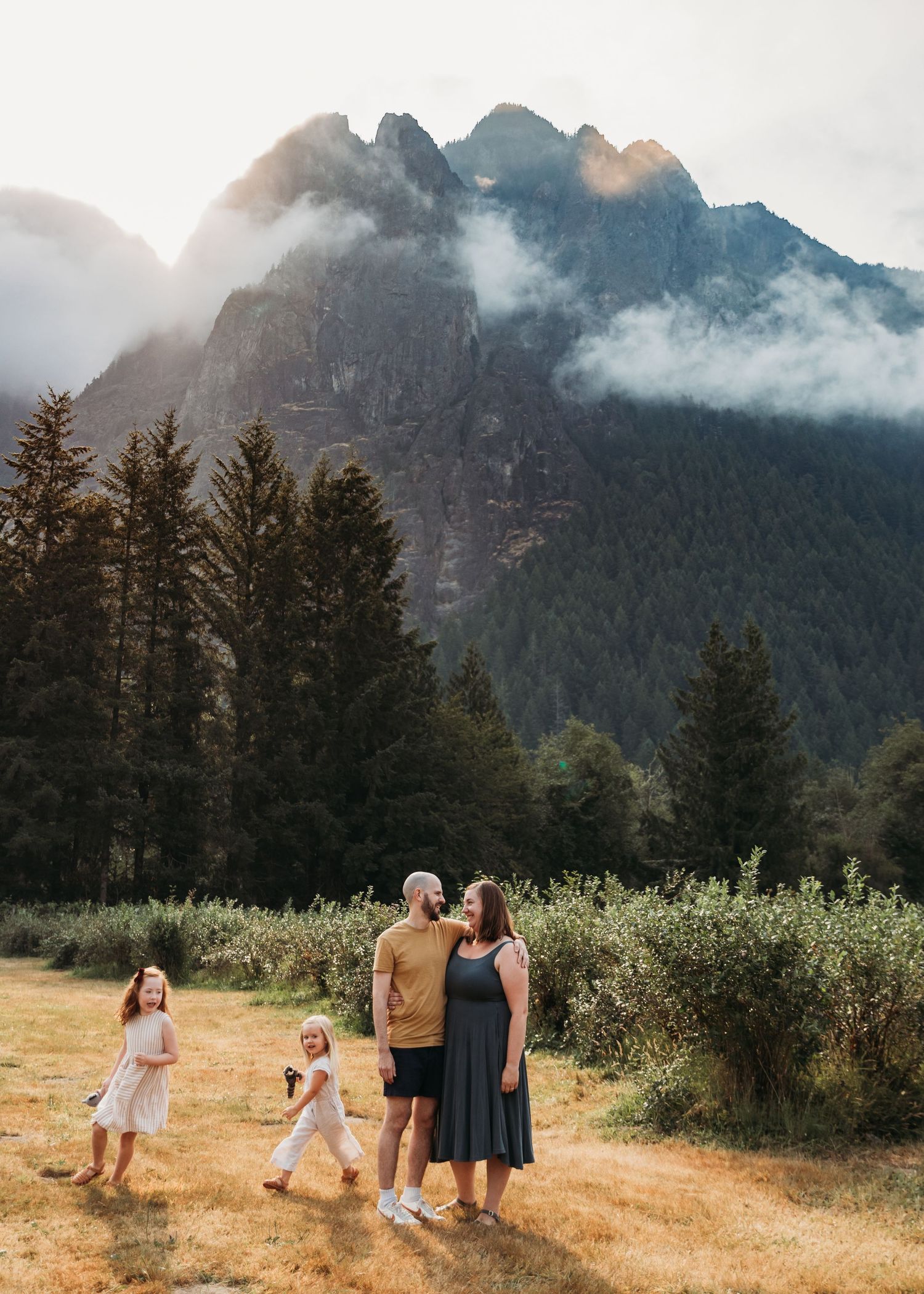 Family enjoying a scenic mountain landscape with misty peaks and evergreen trees in the Pacific Northwest at sunset.