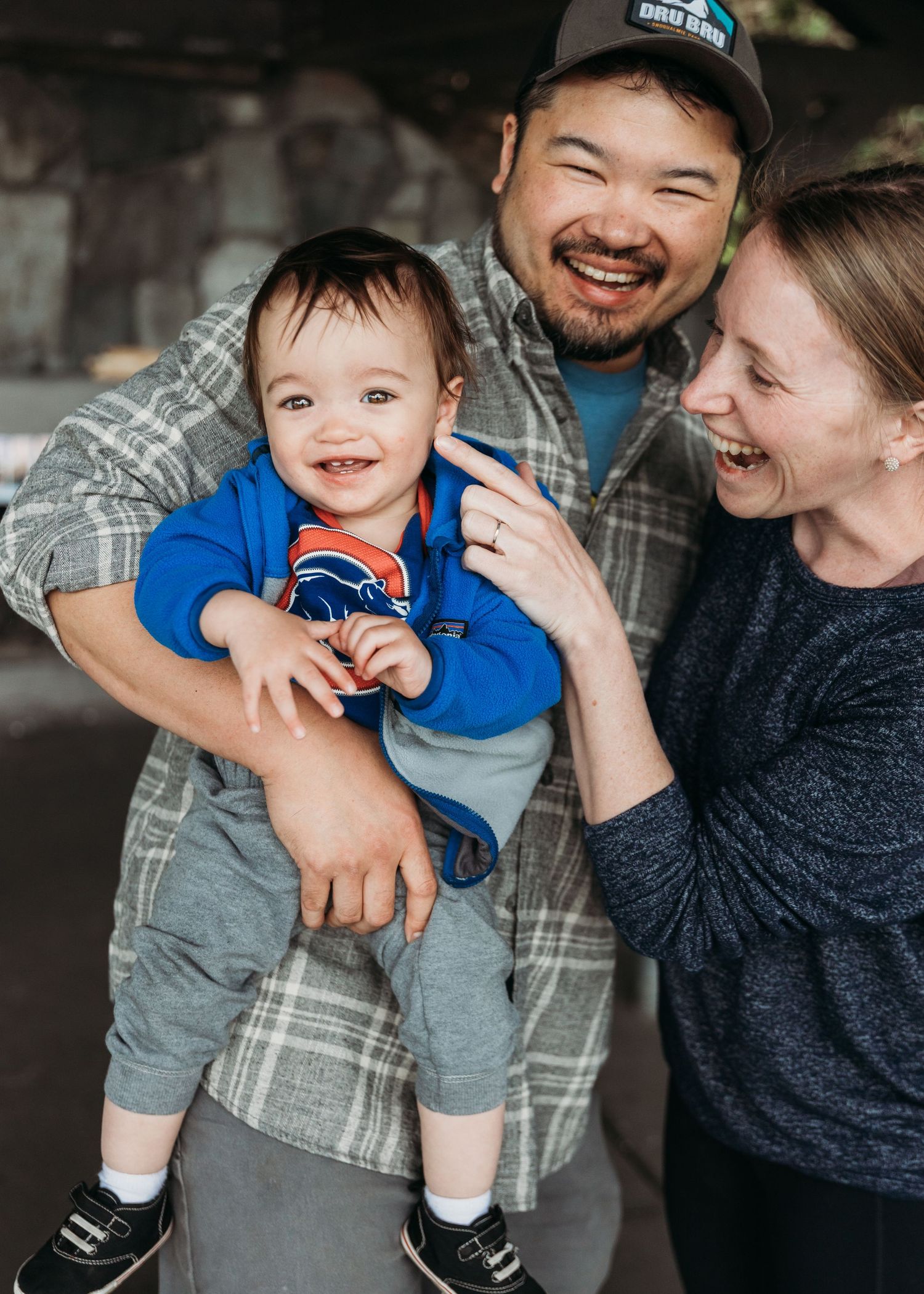 A happy family of three laugh together as they embrace and share a candid moment indoors.
