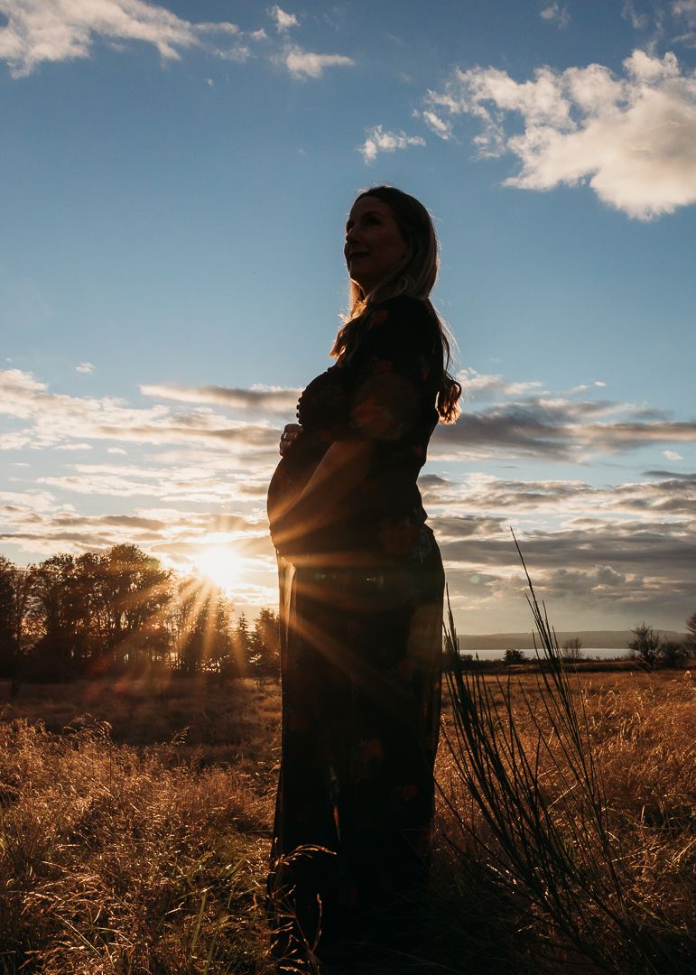 Silhouetted figure stands in golden sunlit field at dusk with dramatic cloudy sky and tall grass in foreground.