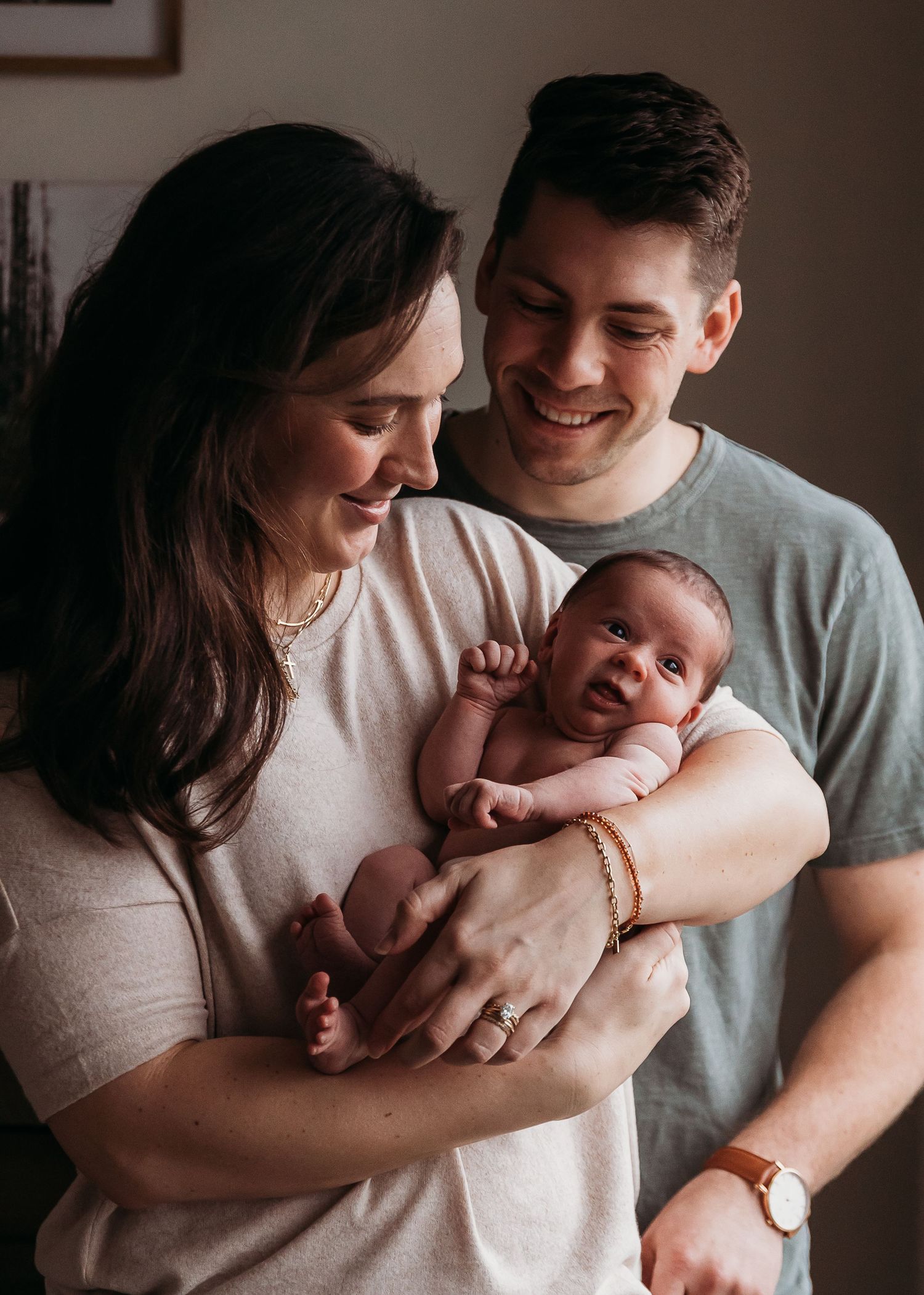A loving couple shares a tender moment while holding their newborn baby in a warmly lit indoor setting.