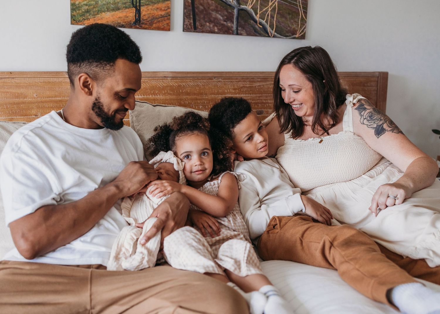 Family relaxing together on bed wearing coordinated white and tan outfits at home.