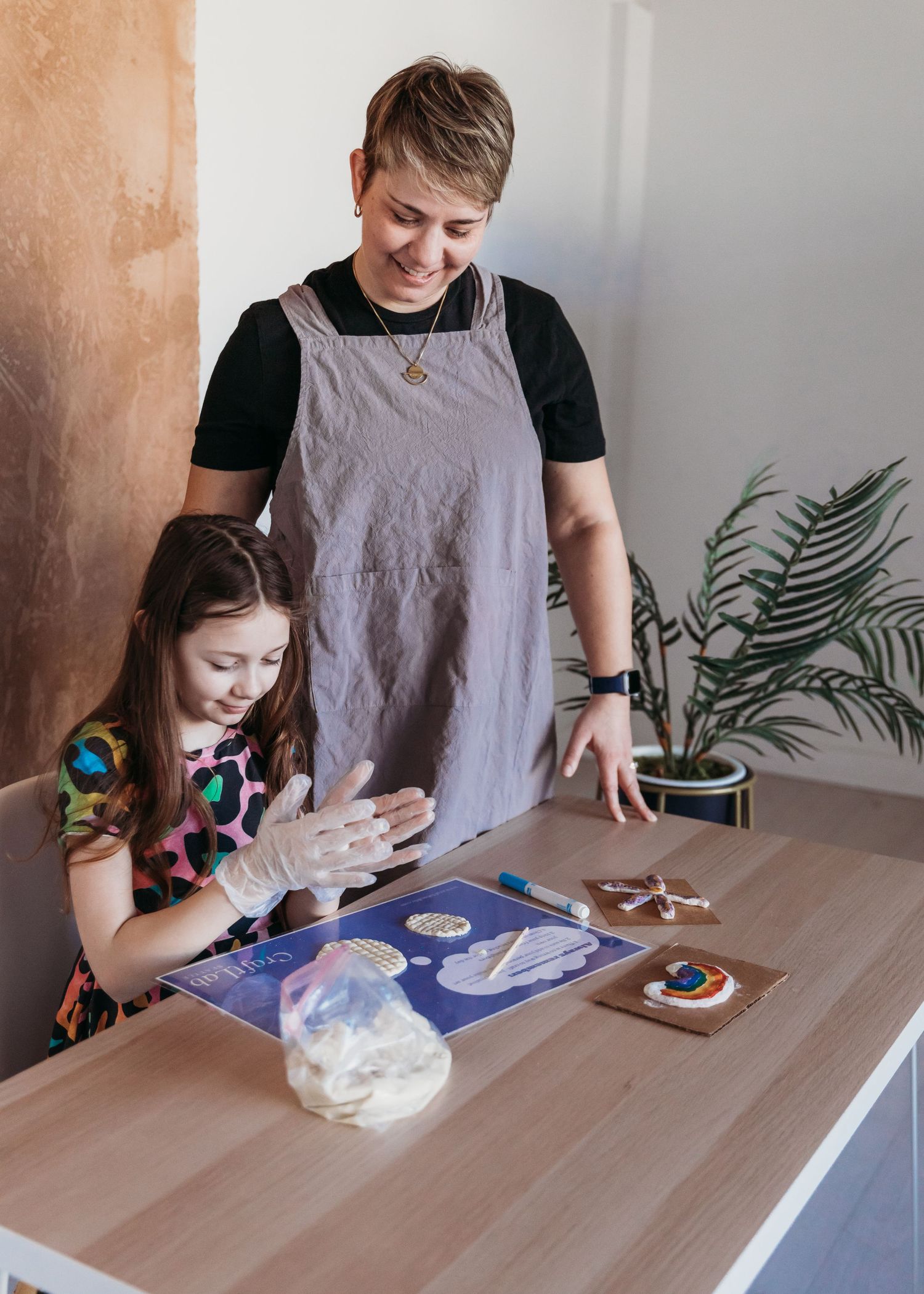 Two people making dough together at a wooden table with a mixing bowl and kitchen supplies, one wearing a gray apron.