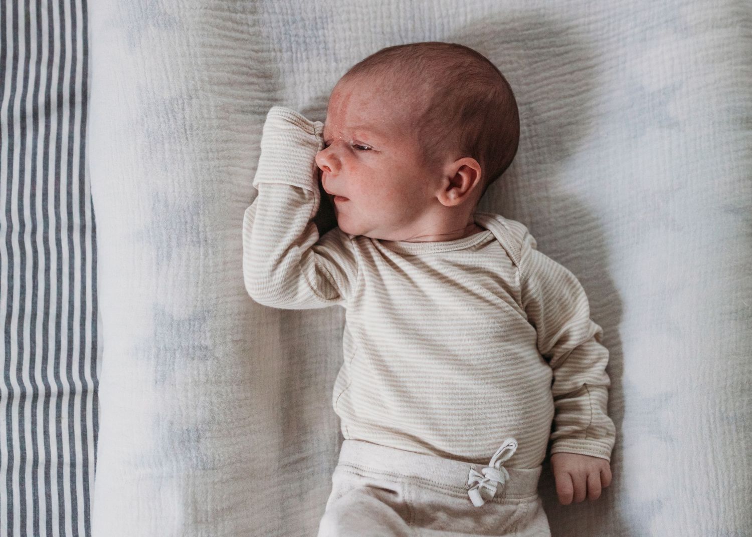 A newborn baby wearing cream-colored clothing lies peacefully on a striped blanket.