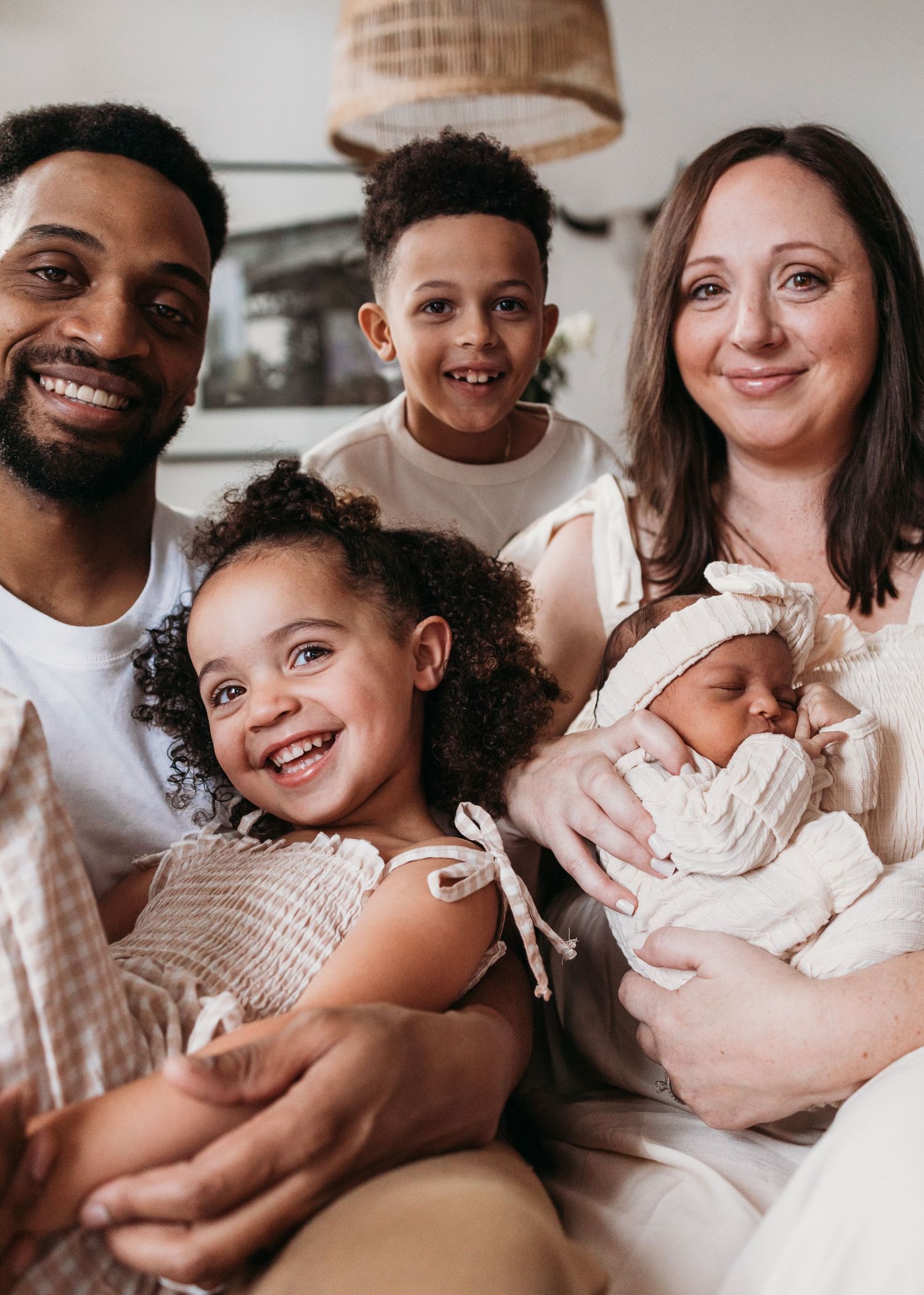 A loving mixed family sitting together at home with their newborn baby in warm, natural light.