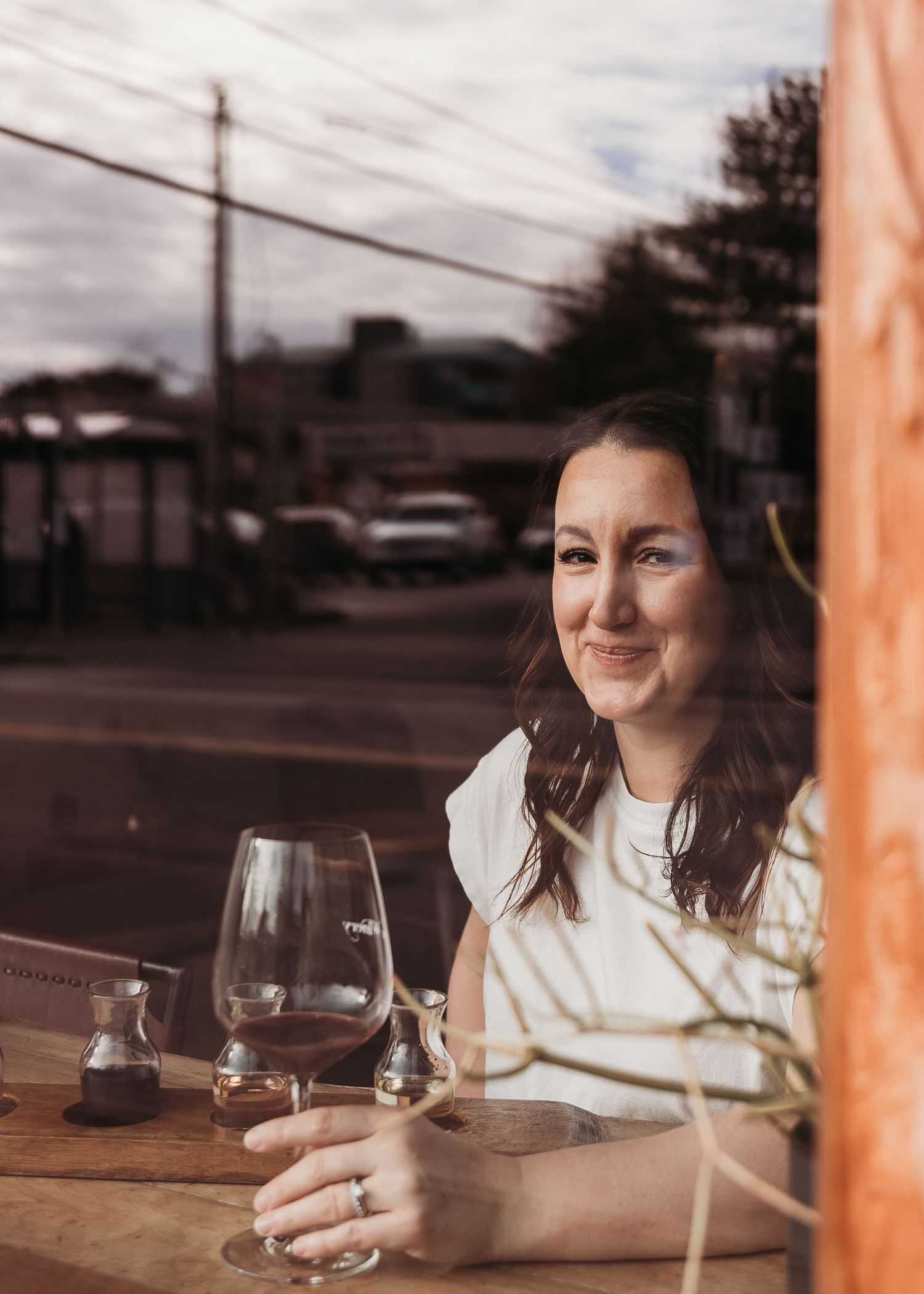 View through window of person enjoying red wine at wooden table in warm evening lighting.