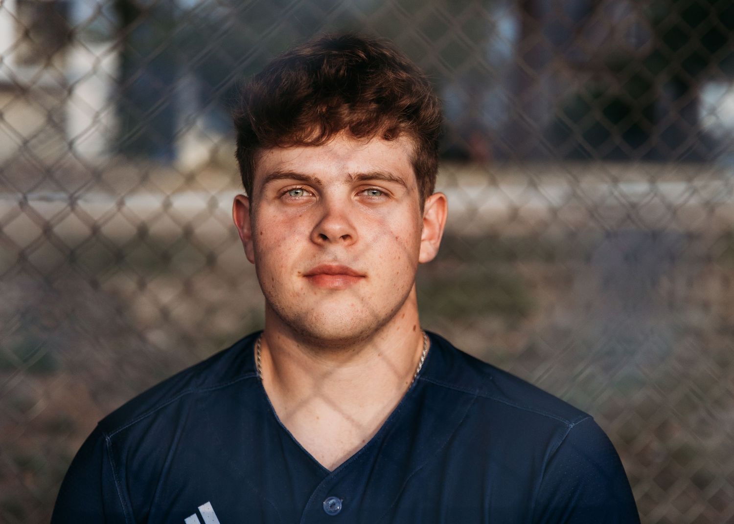 Portrait of a young athlete in a navy blue athletic shirt against a chain link fence background.