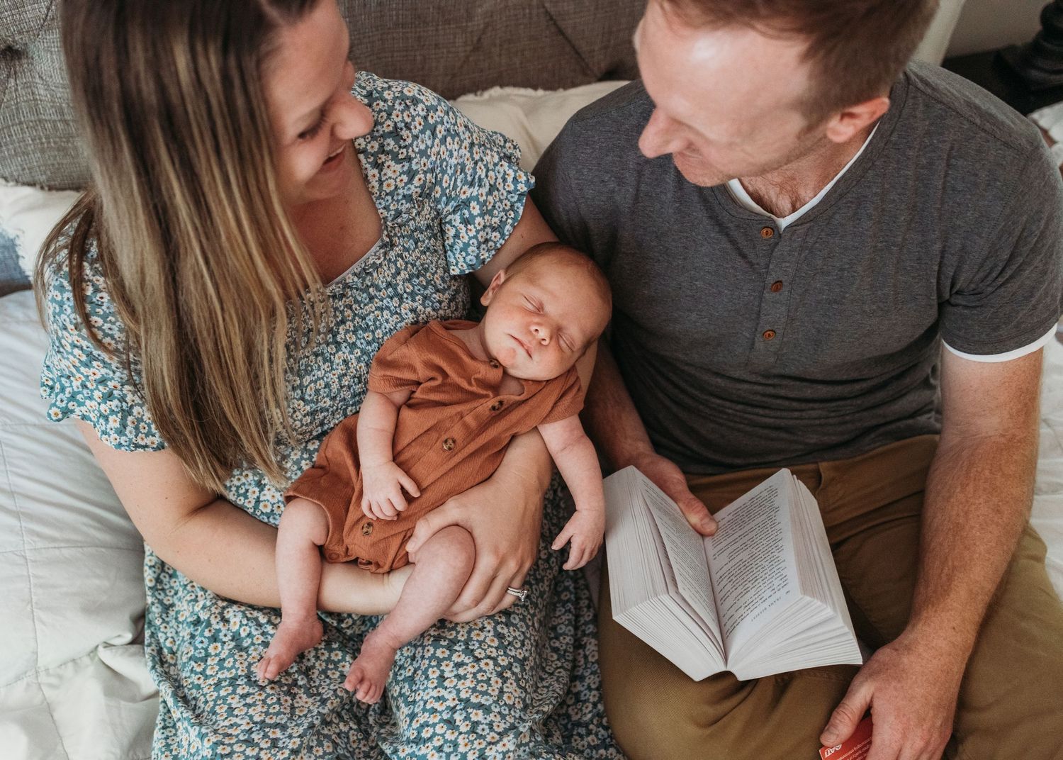 Parents sharing tender moment with newborn baby at home while sitting on couch during reading.