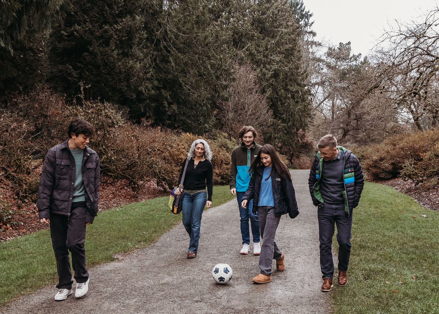 A group of young friends walk together on a park trail with a soccer ball on an overcast autumn day.
