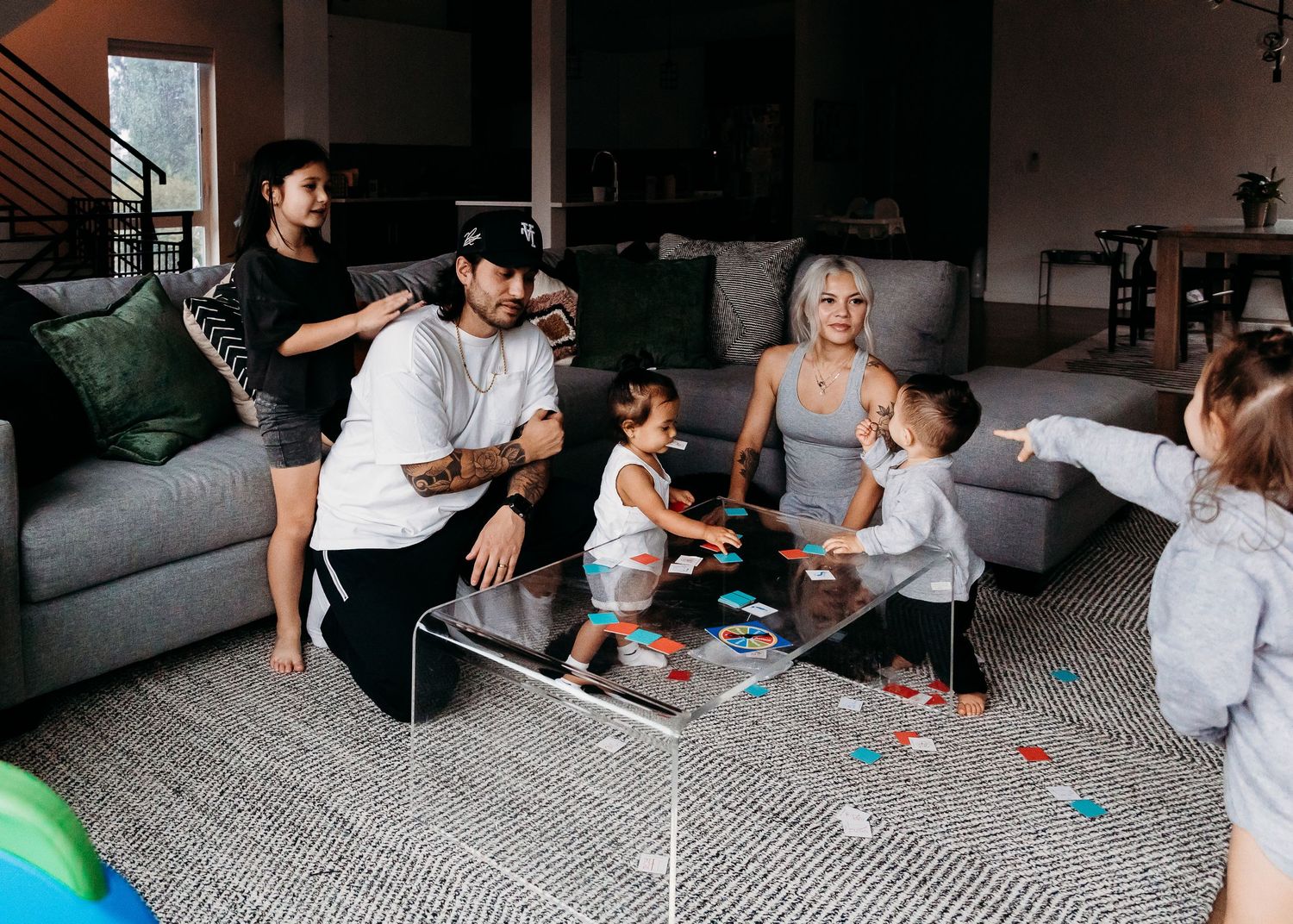 A family gathers in their living room playing on the floor with colorful toys and games together.