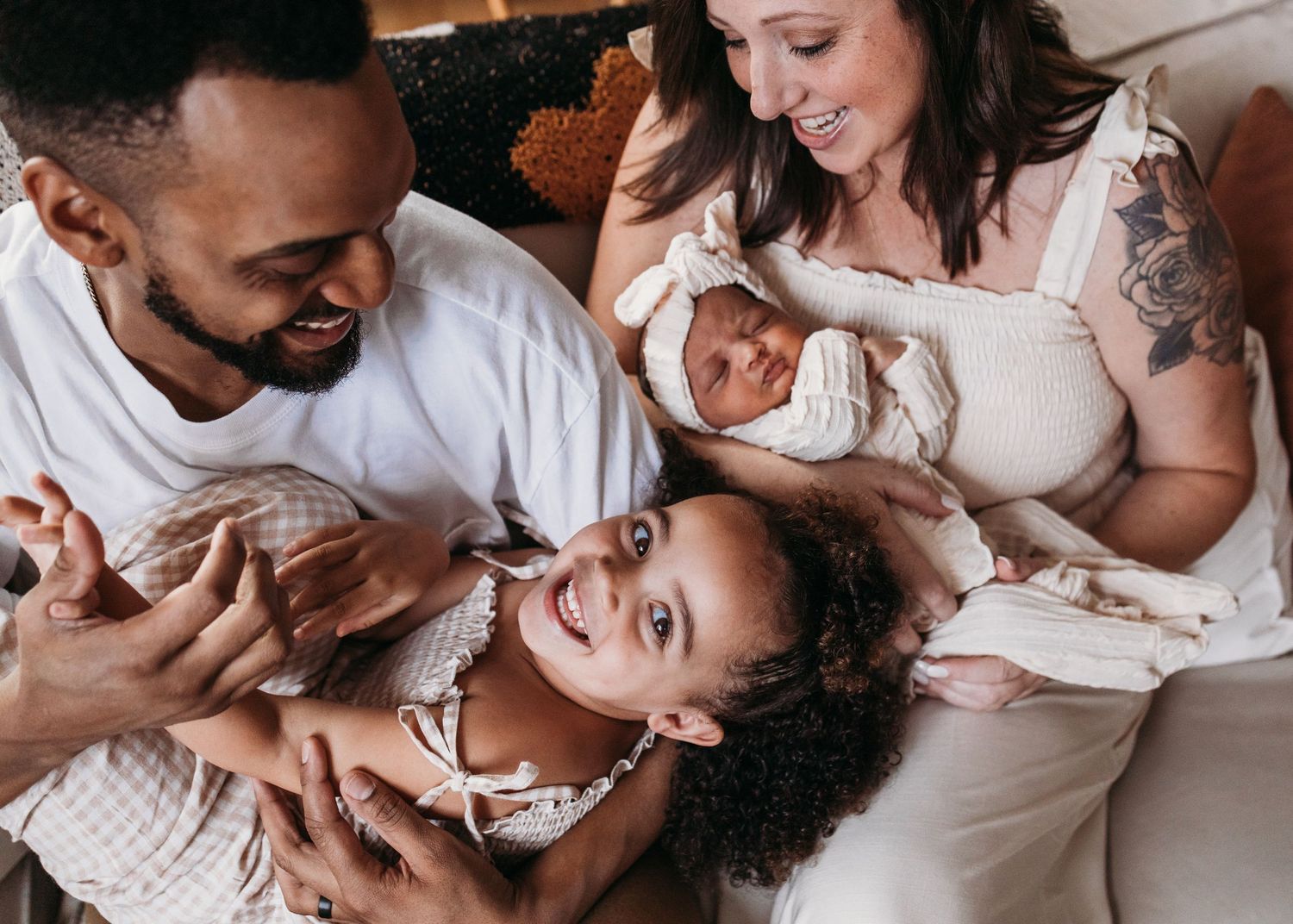 Happy family in white clothing lying down together while cuddling with their two young children.