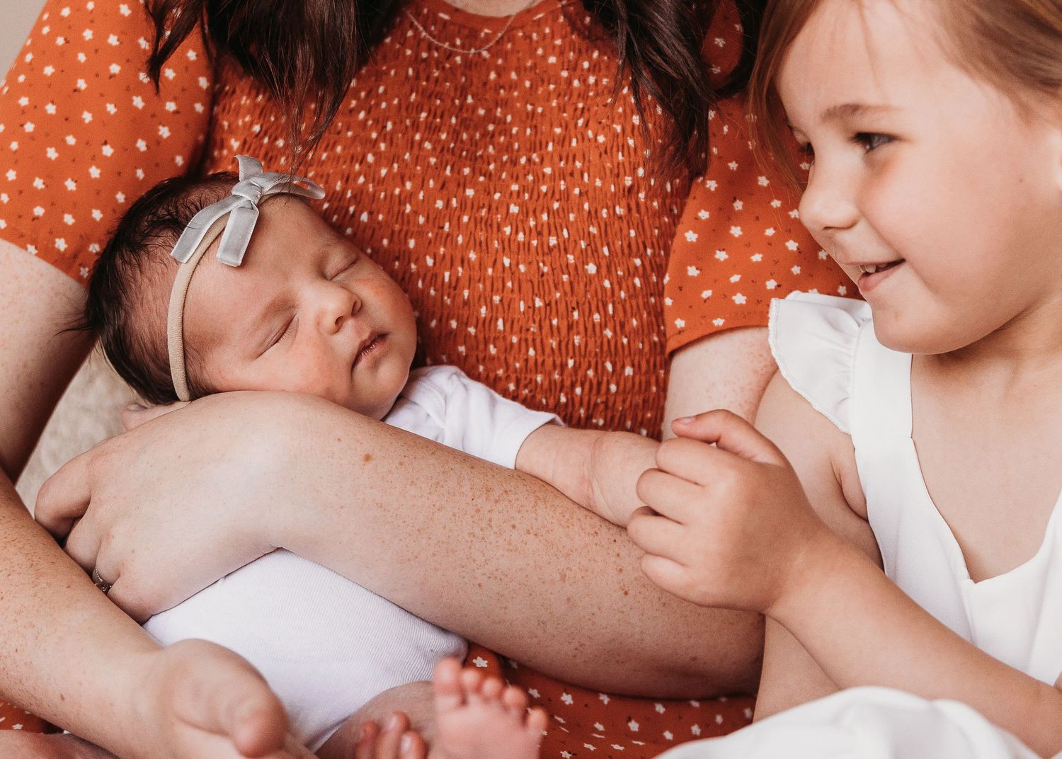 A sleeping baby in white clothing rests peacefully next to another child wearing white on a polka dot pattern.