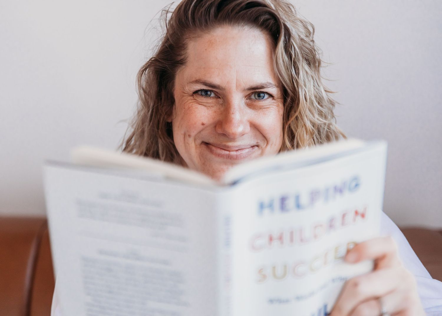 Someone holding and reading a book titled 'Helping Children Succeed' with a warm expression.
