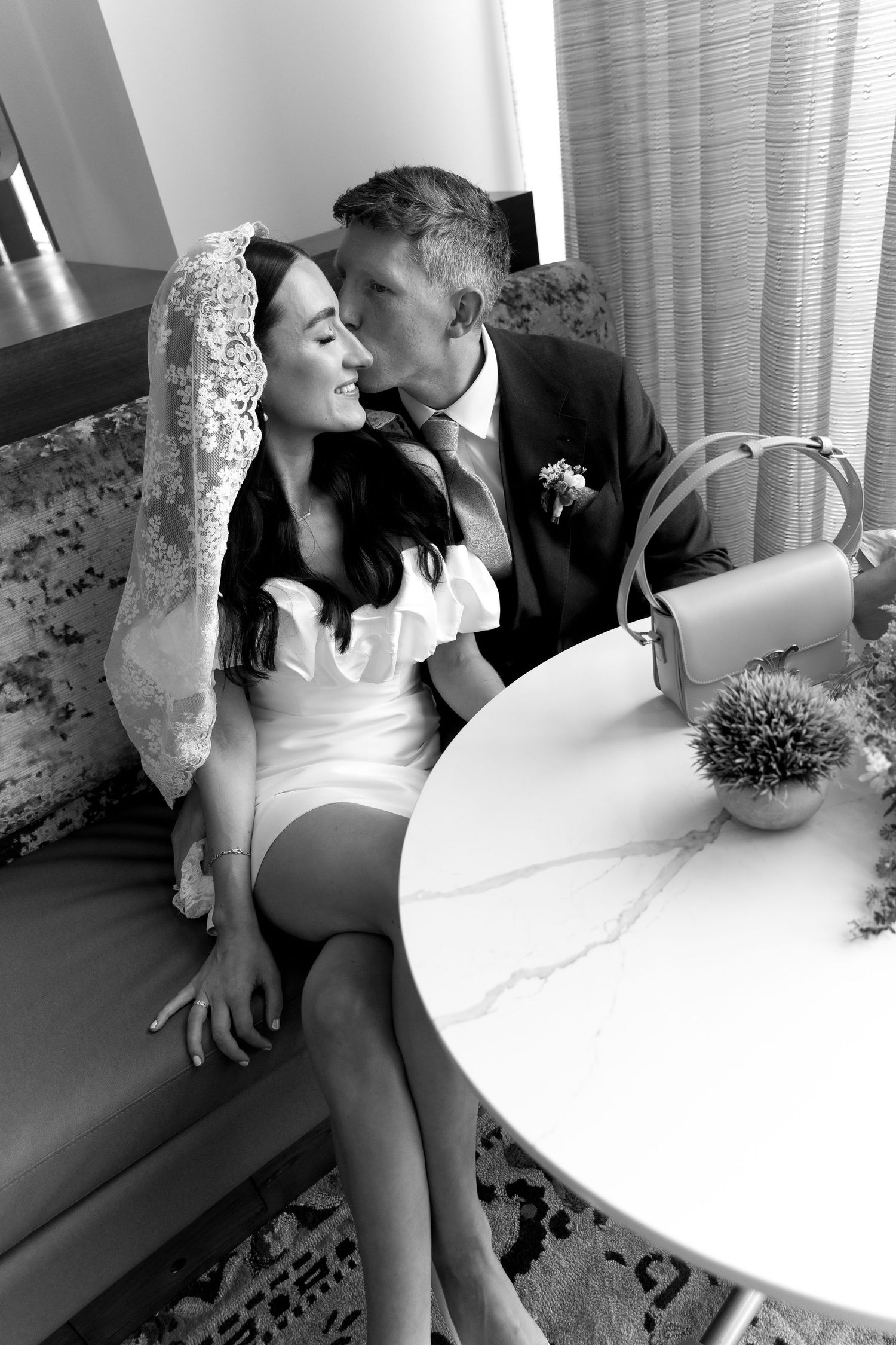 A wedding couple shares romantic moments sitting and kissing on a couch in a series of black and white photographs.