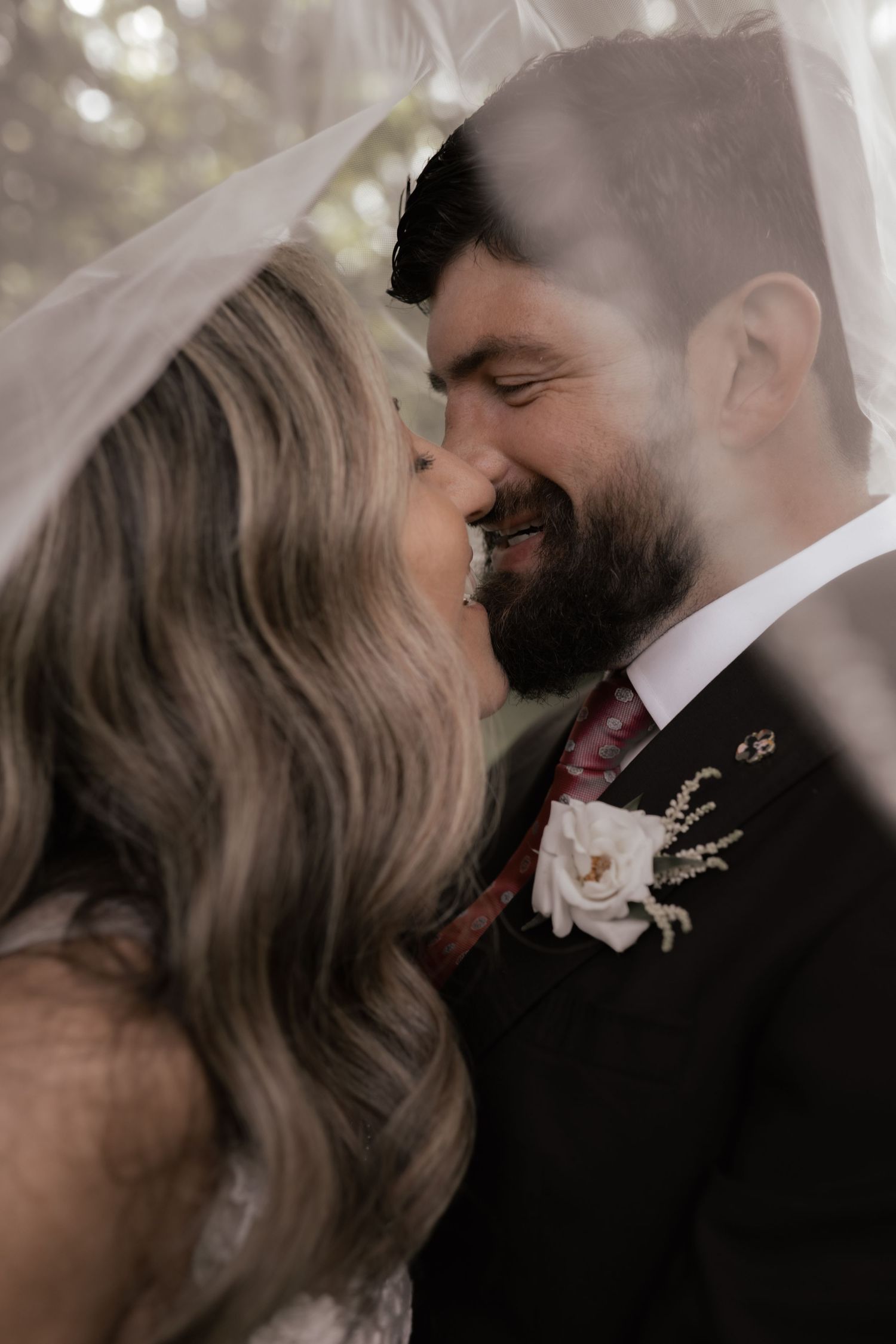 Intimate wedding portrait of couple under a delicate veil with soft romantic lighting.