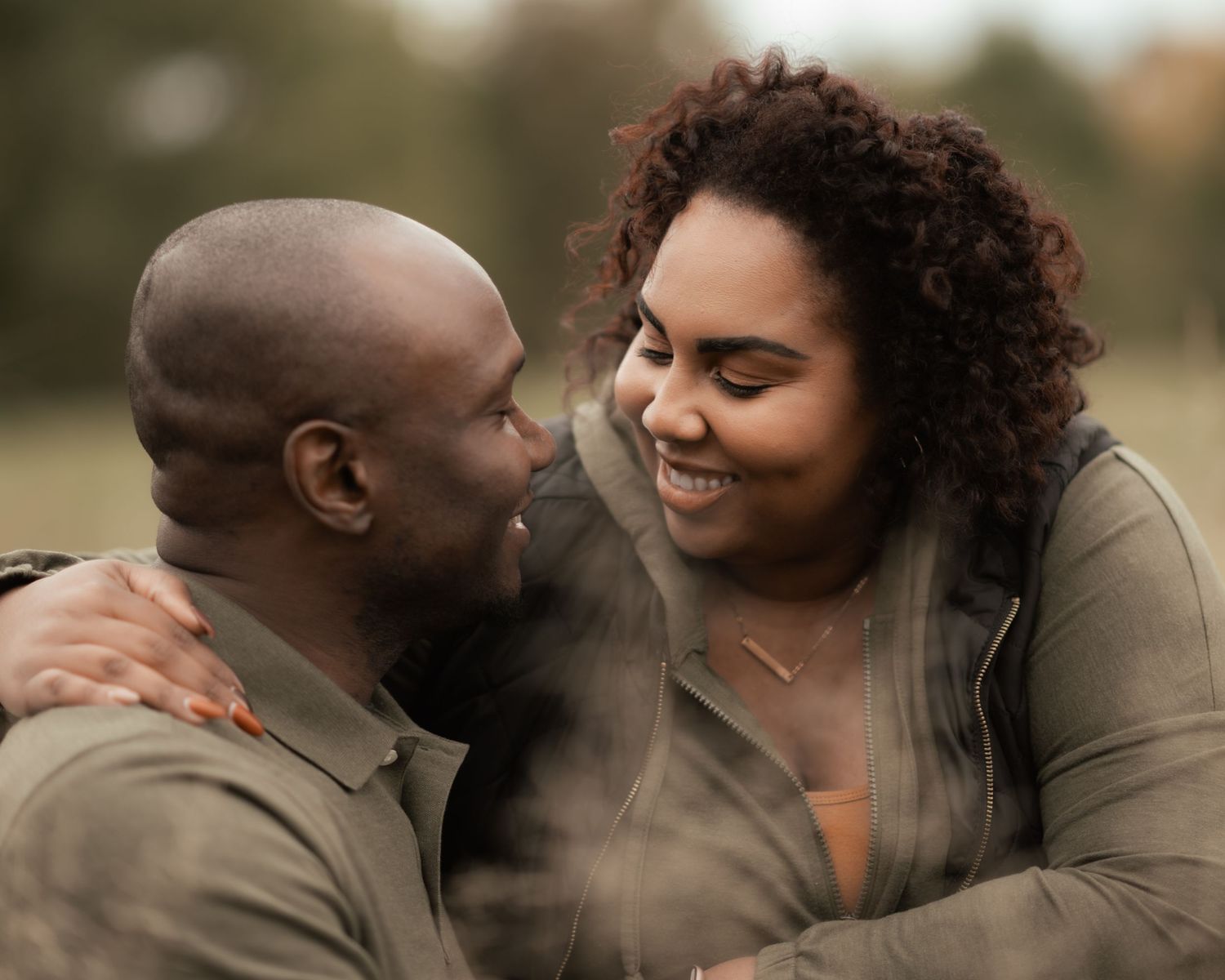 Couple laughing together while embracing in a field of tall grass during sunset.