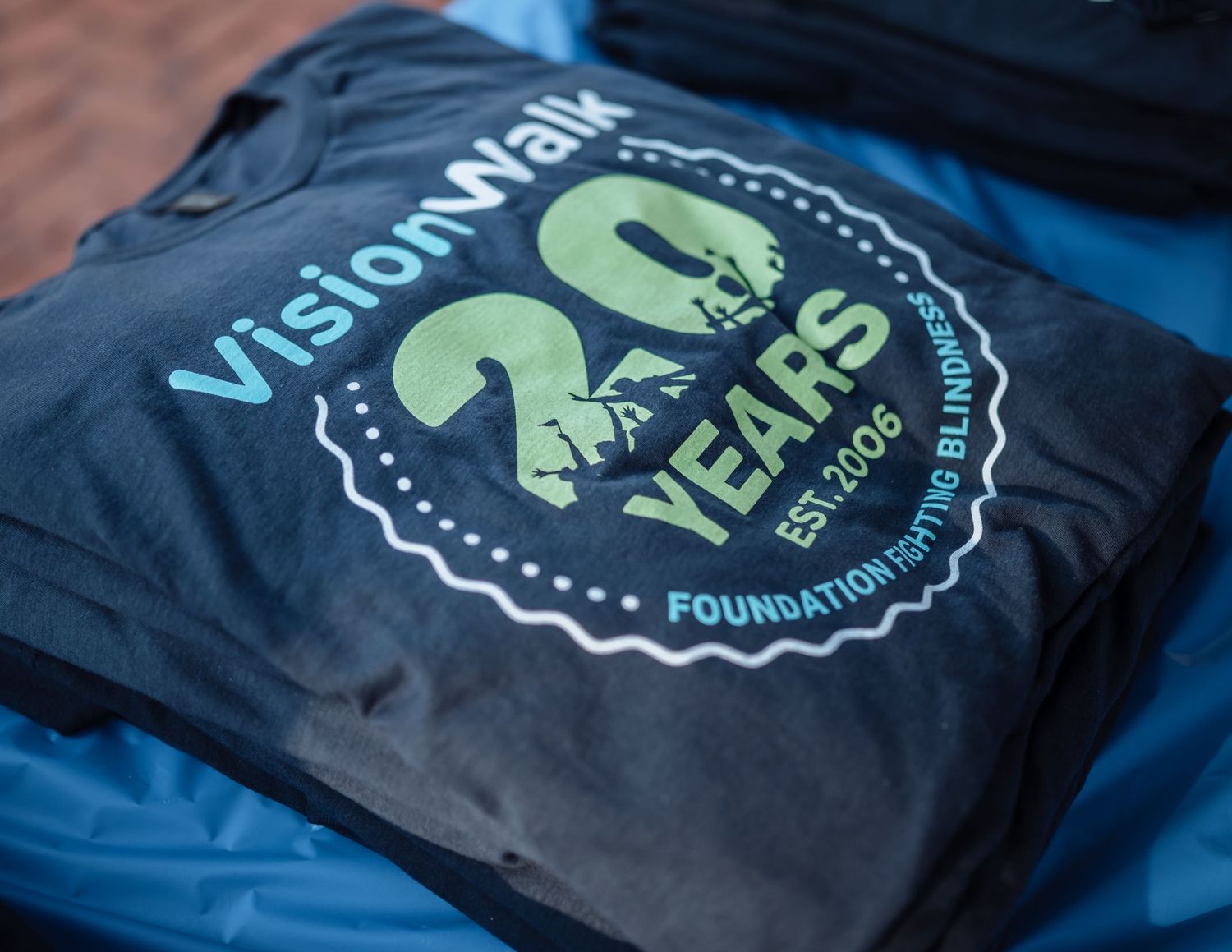 A series of black t-shirts with green and white logo designs displayed in a row.